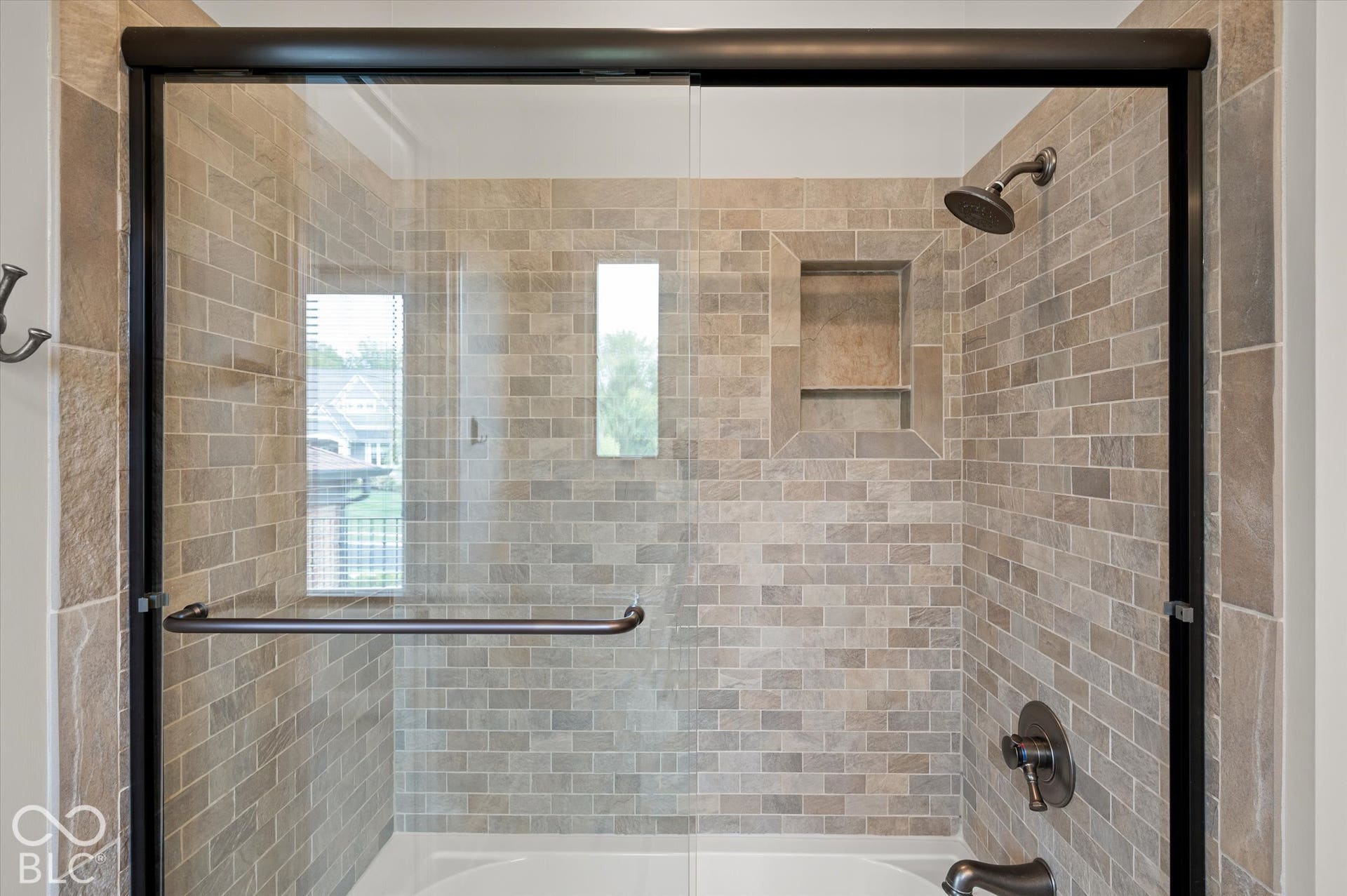 Shower with glass enclosure, subway tile surround, built-in niche, and bronze fixtures