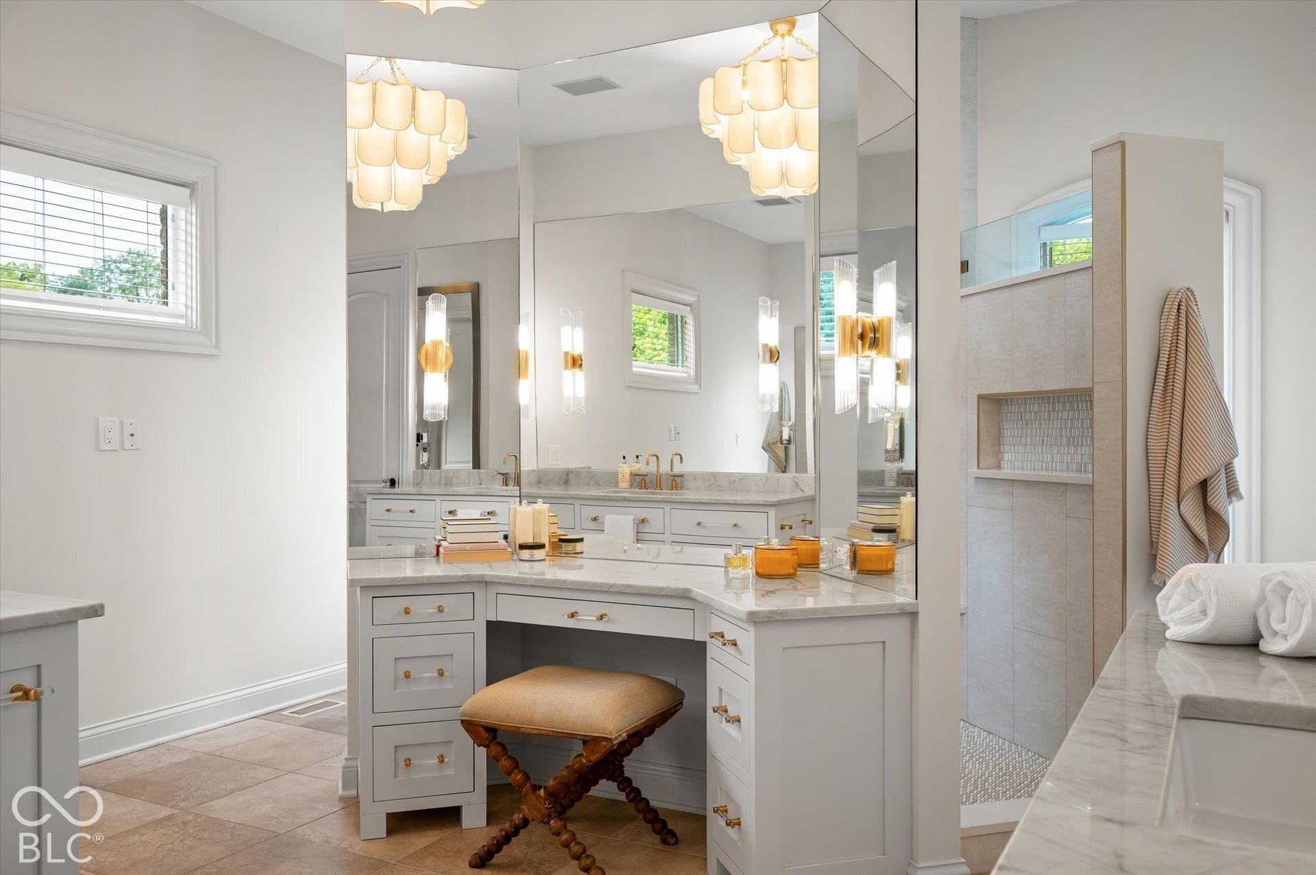 Integrated vanity station with a stone countertop, elegant wall sconces, a tiled walk-in shower with a recessed niche, and a large mirror