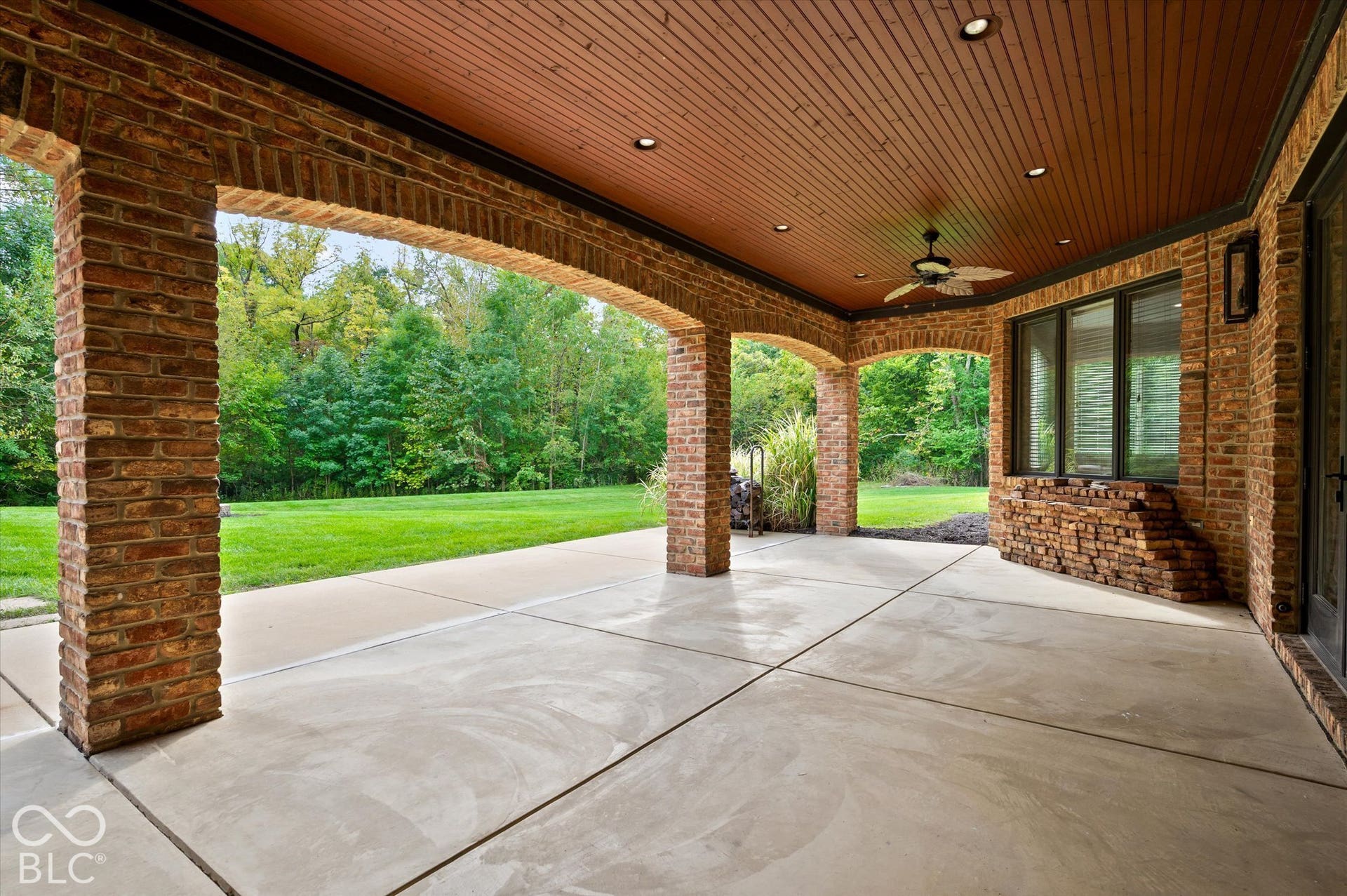 Expansive covered patio featuring brick archways, a wood-finish ceiling with recessed lighting, a ceiling fan, and a stone-clad window sill