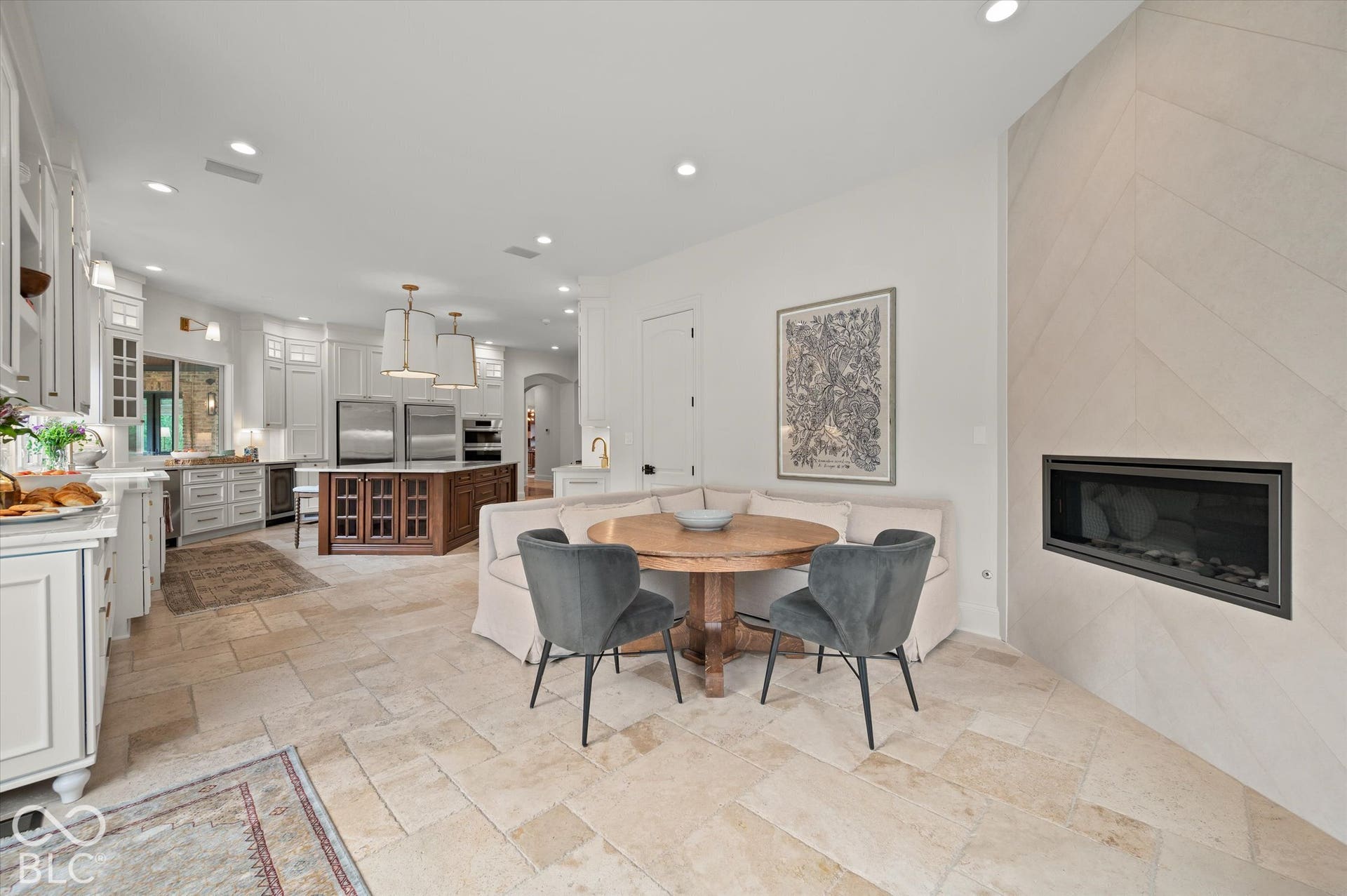 Recessed fireplace with chevron-patterned surround, tiled flooring, wood-finish kitchen island, and white shaker cabinetry