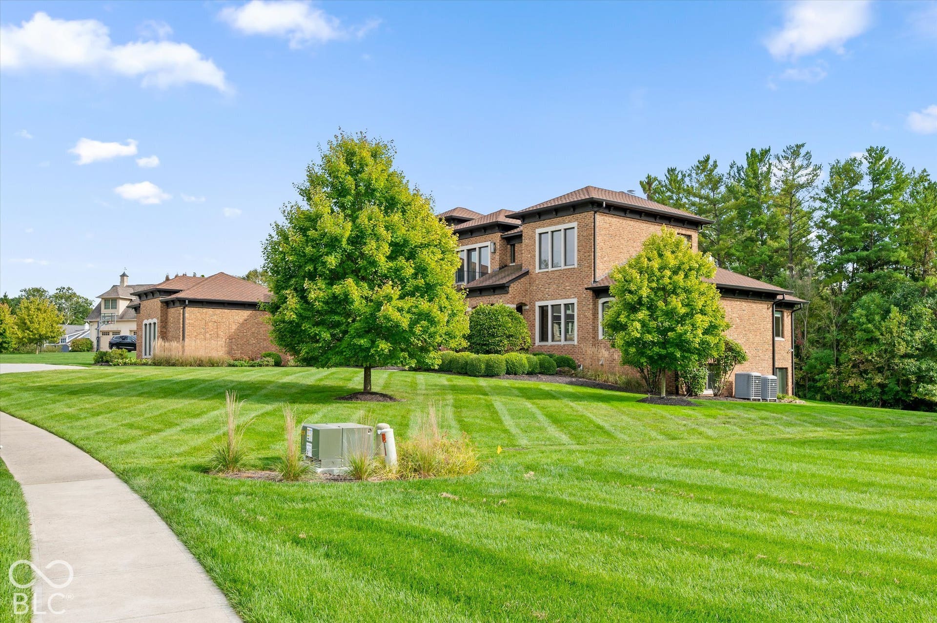 Brick exterior with multiple windows, surrounded by mature trees and manicured lawn