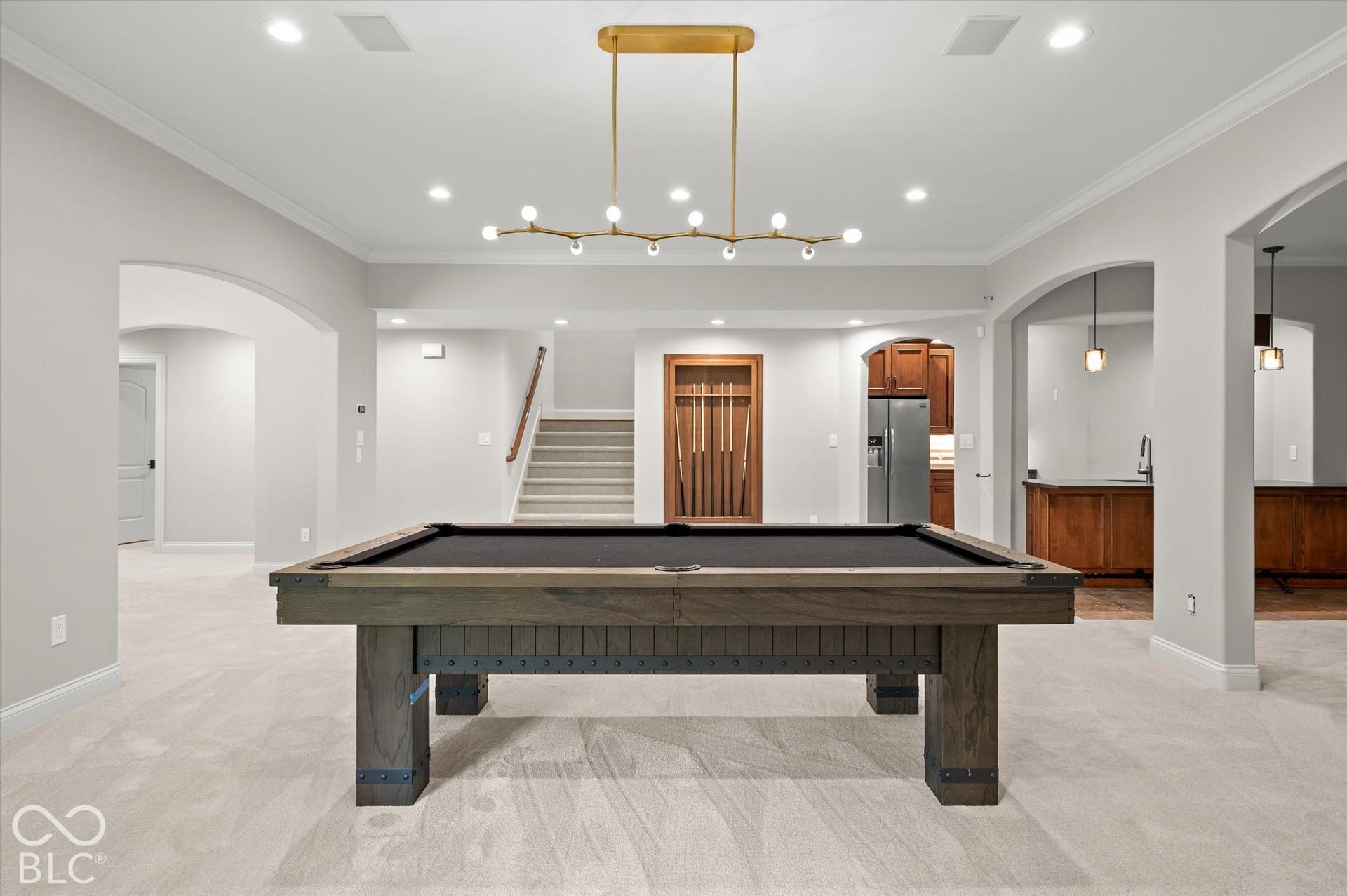 Recreation room with recessed lighting, a modern linear chandelier, arched doorways, a built-in cue rack, and a wet bar featuring wood cabinetry