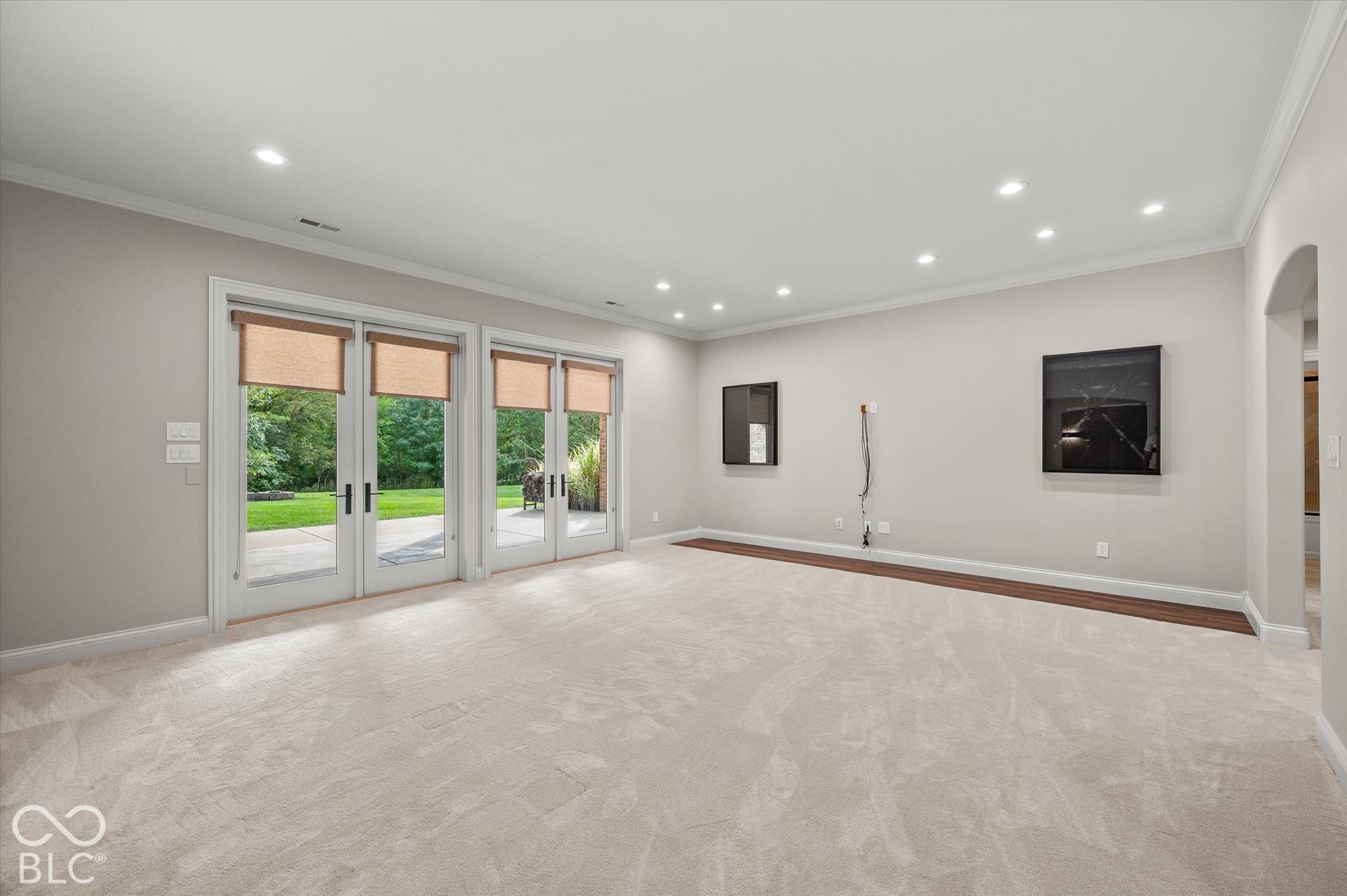 Recessed lighting, light-toned carpeting, two sets of French patio doors with roller shades, and an arched entryway