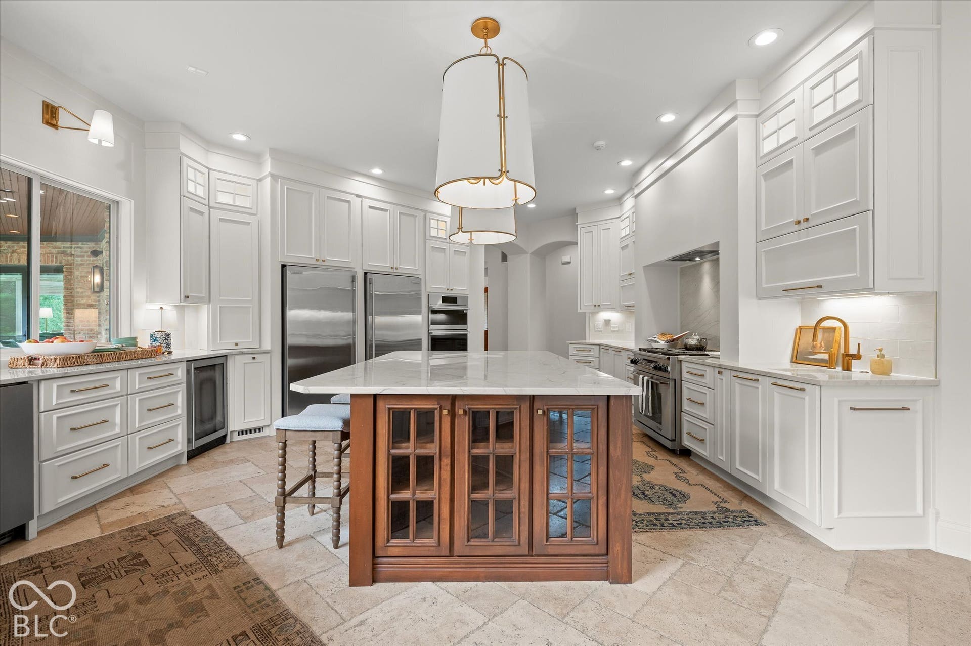 Spacious kitchen featuring white cabinetry, integrated stainless steel appliances, a large center island with a wood base and stone countertop, and tile flooring