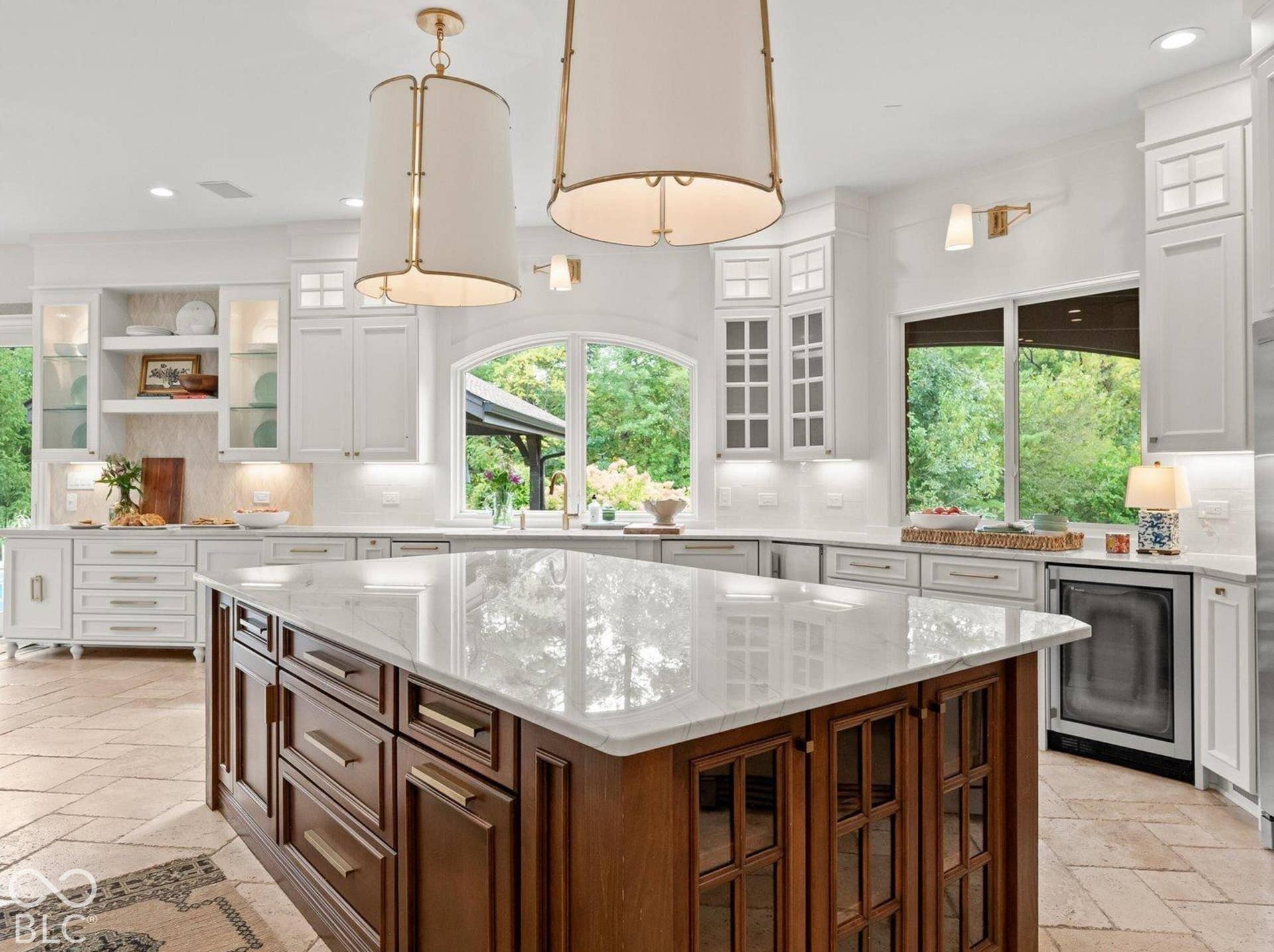 Expansive kitchen featuring a large wood-finish island with a light-toned countertop, white cabinetry, and two prominent pendant lights