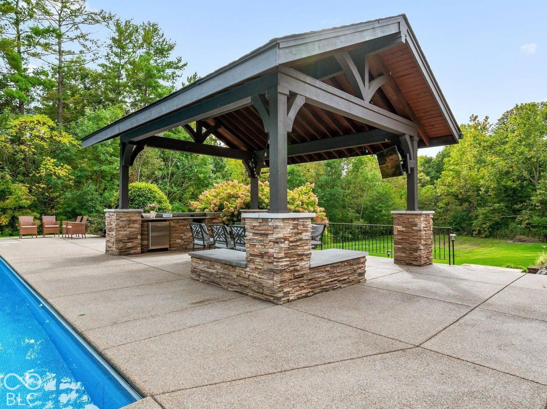 Expansive outdoor living area featuring a covered patio, exposed aggregate concrete decking, and a built-in stone seating area