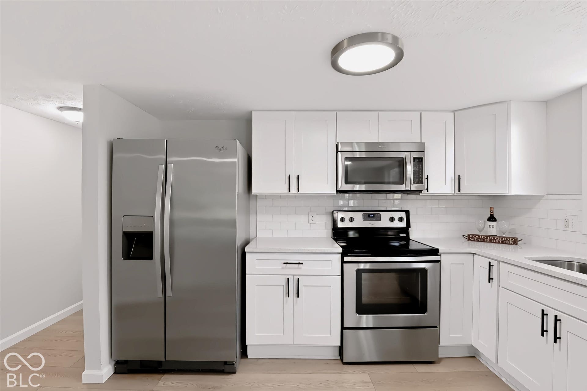 White cabinetry with matte black hardware, stainless steel appliances, white subway tile backsplash, light-toned countertops, and wood-finish flooring