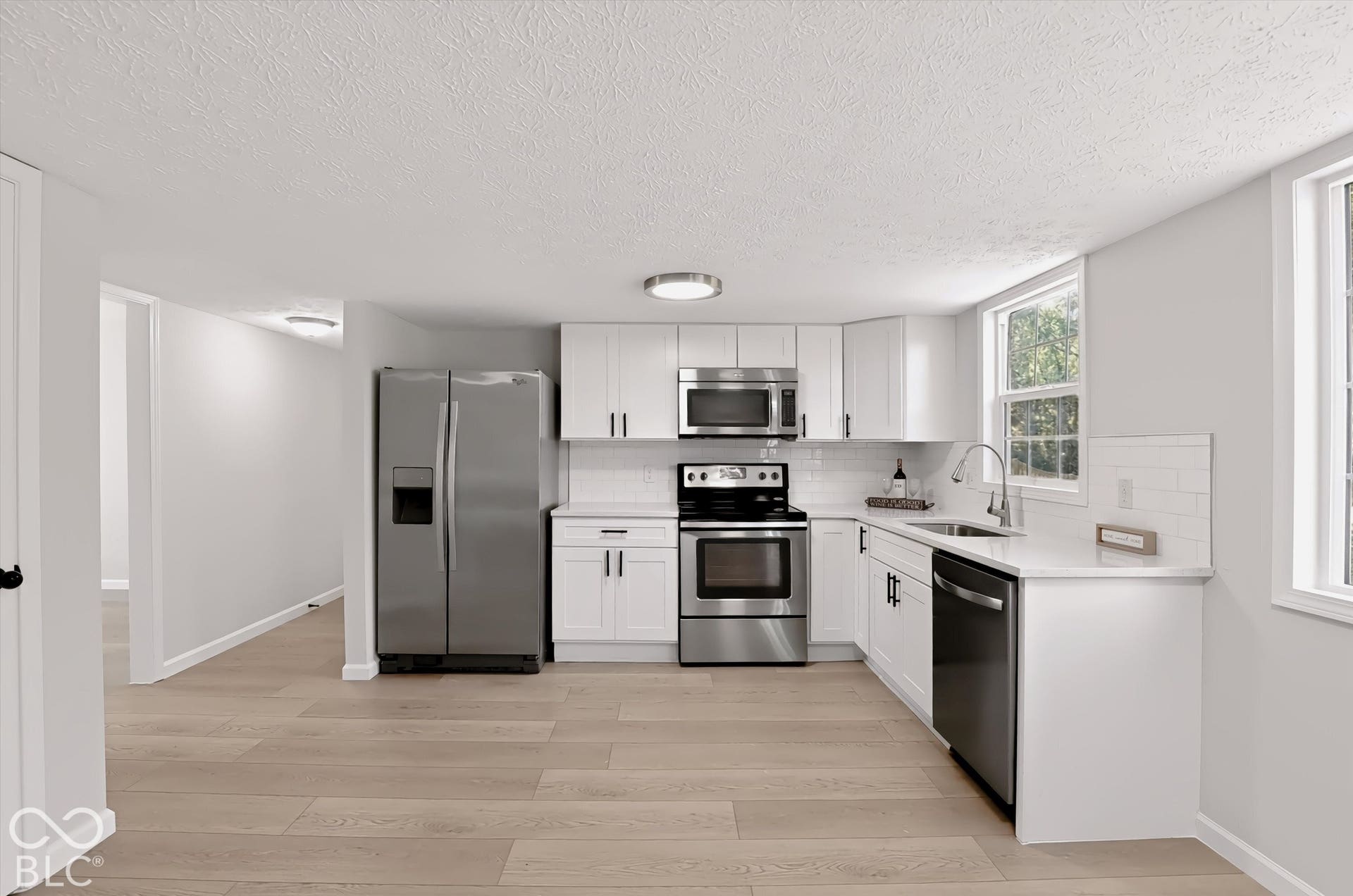 Kitchen featuring wood-finish flooring, white cabinetry, stainless steel appliances, white subway tile backsplash, and light-toned countertops