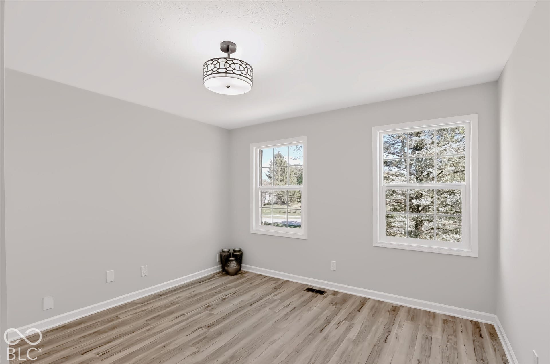 Wood-finish flooring, two large windows with white trim, and a decorative semi-flush mount ceiling fixture