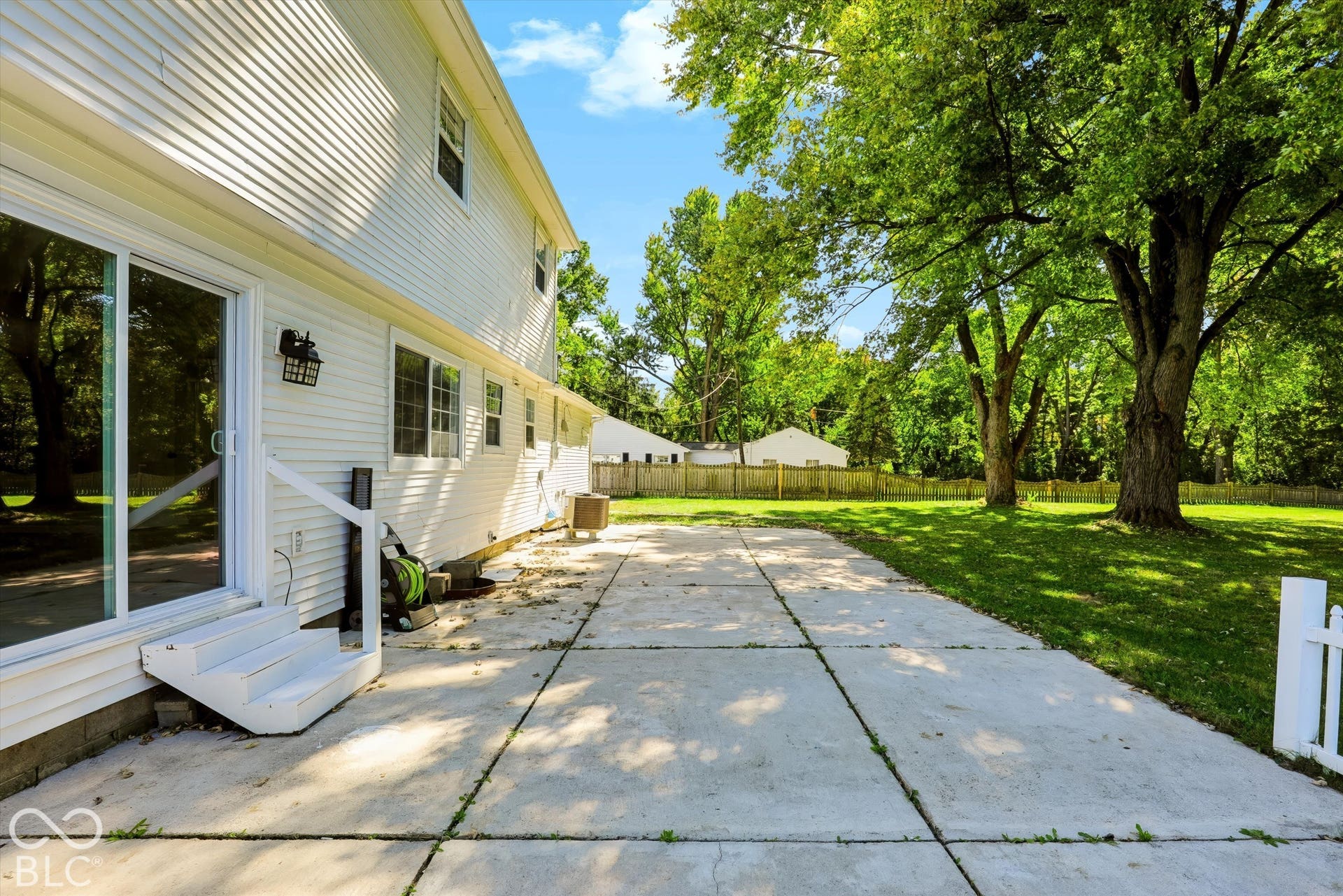 Expansive concrete patio with direct access to the exterior, featuring a sliding glass door and white vinyl siding
