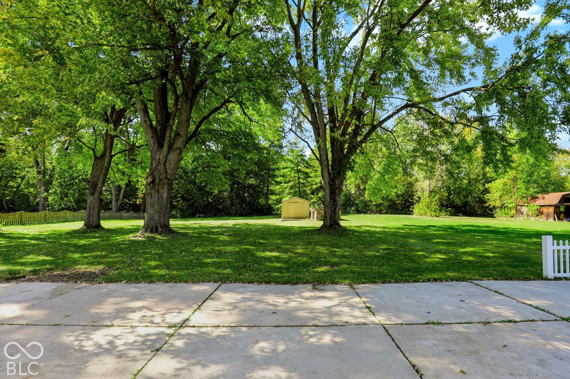 Expansive green lawn with mature trees, a detached storage shed, and a white picket fence detail
