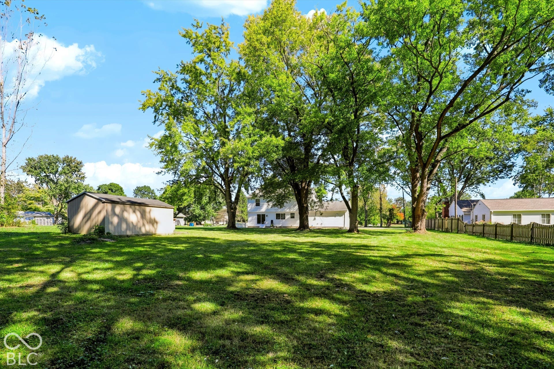 Expansive lawn with mature trees, a detached storage shed, and a wooden picket fence