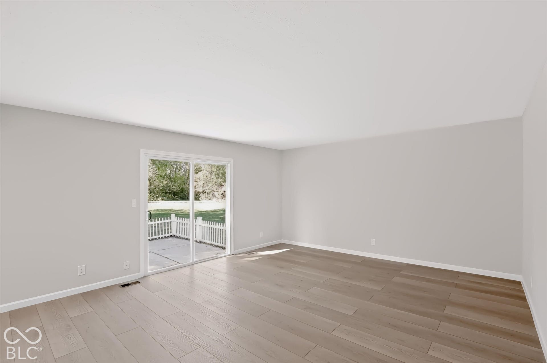 Light wood-finish flooring, light gray walls, white trim, and a sliding glass door opening to an outdoor patio with a white picket fence