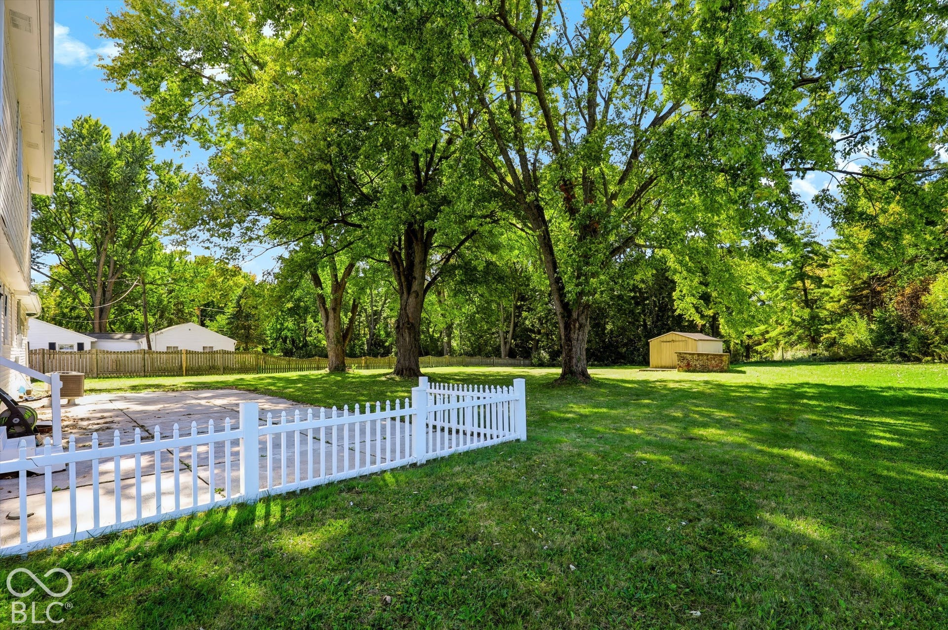 Expansive lawn featuring mature trees and a white picket fence