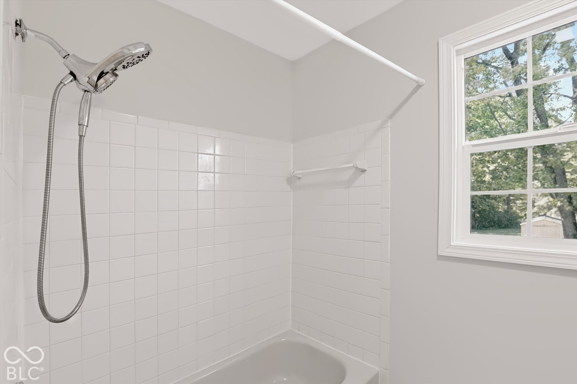 White tile shower surround with a chrome shower head and a single-pane window