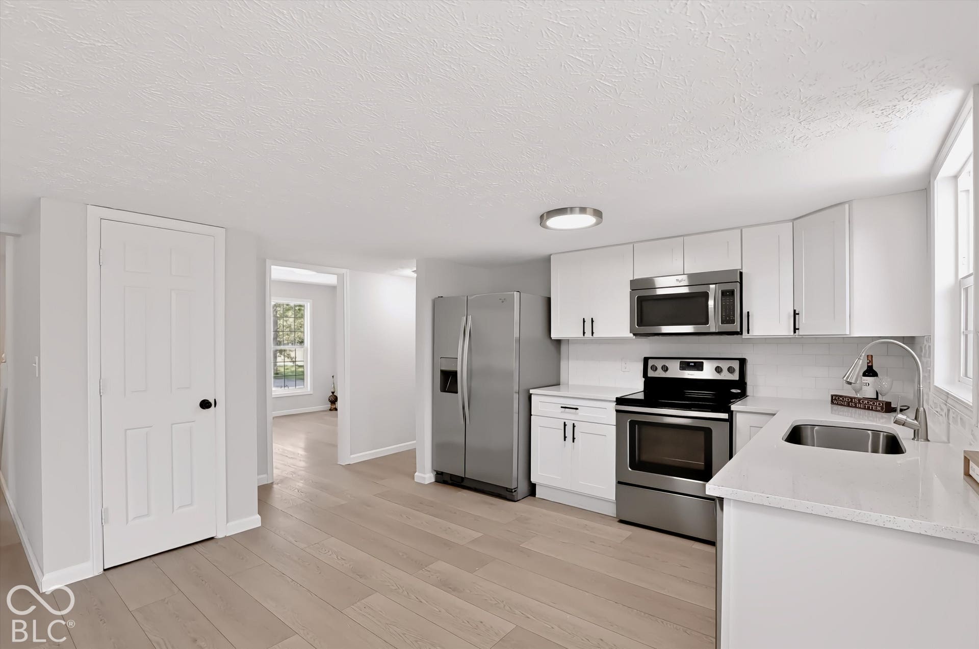 Kitchen featuring stainless steel appliances, white cabinetry, solid surface countertops, a white subway tile backsplash, and light wood-finish flooring