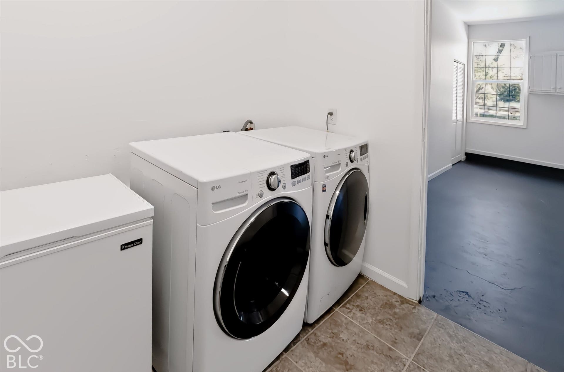 Tiled flooring, white walls, and a separate utility room with a window and built-in white cabinetry