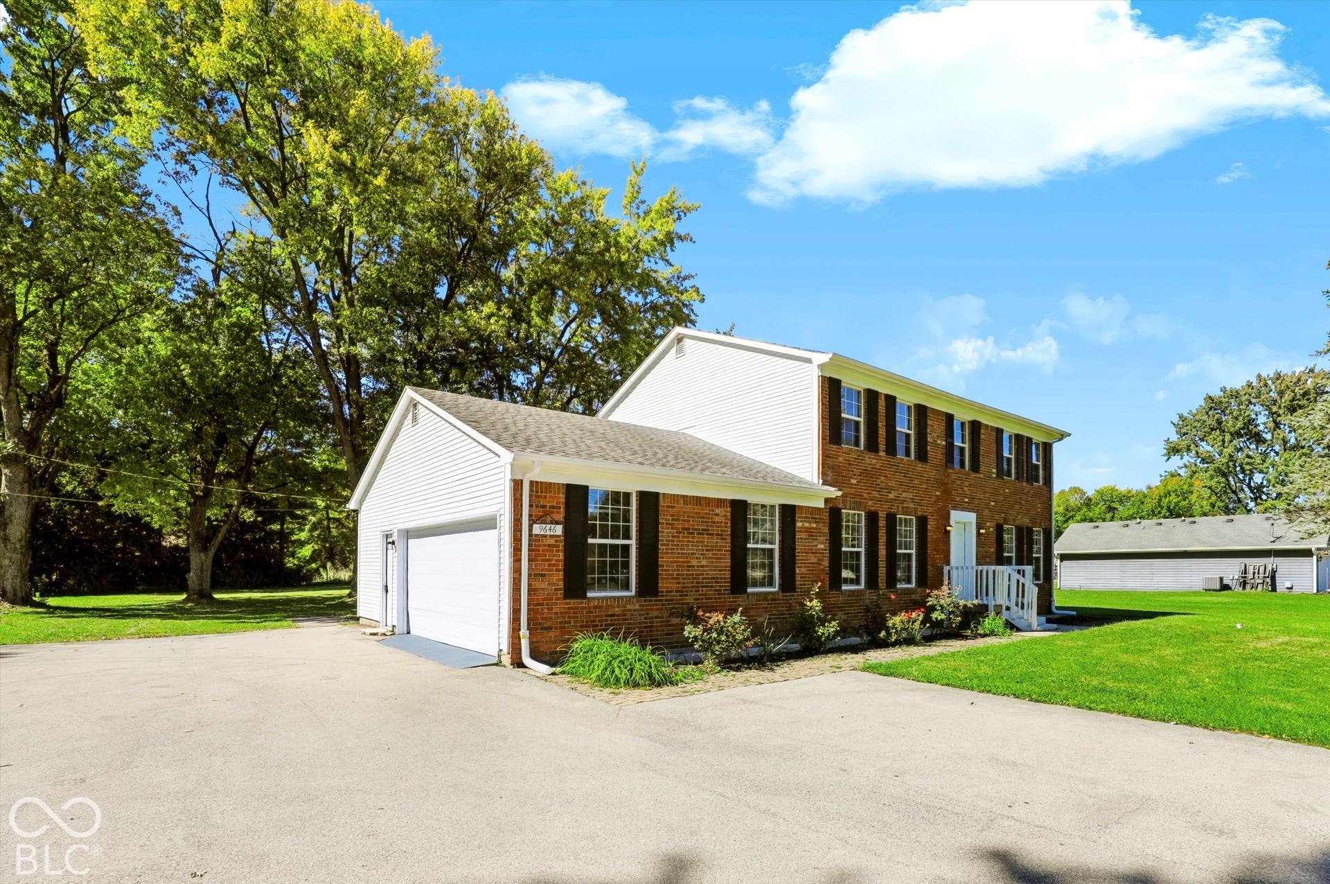 Brick and siding exterior with dark shutters, attached garage, white front porch, and paved driveway