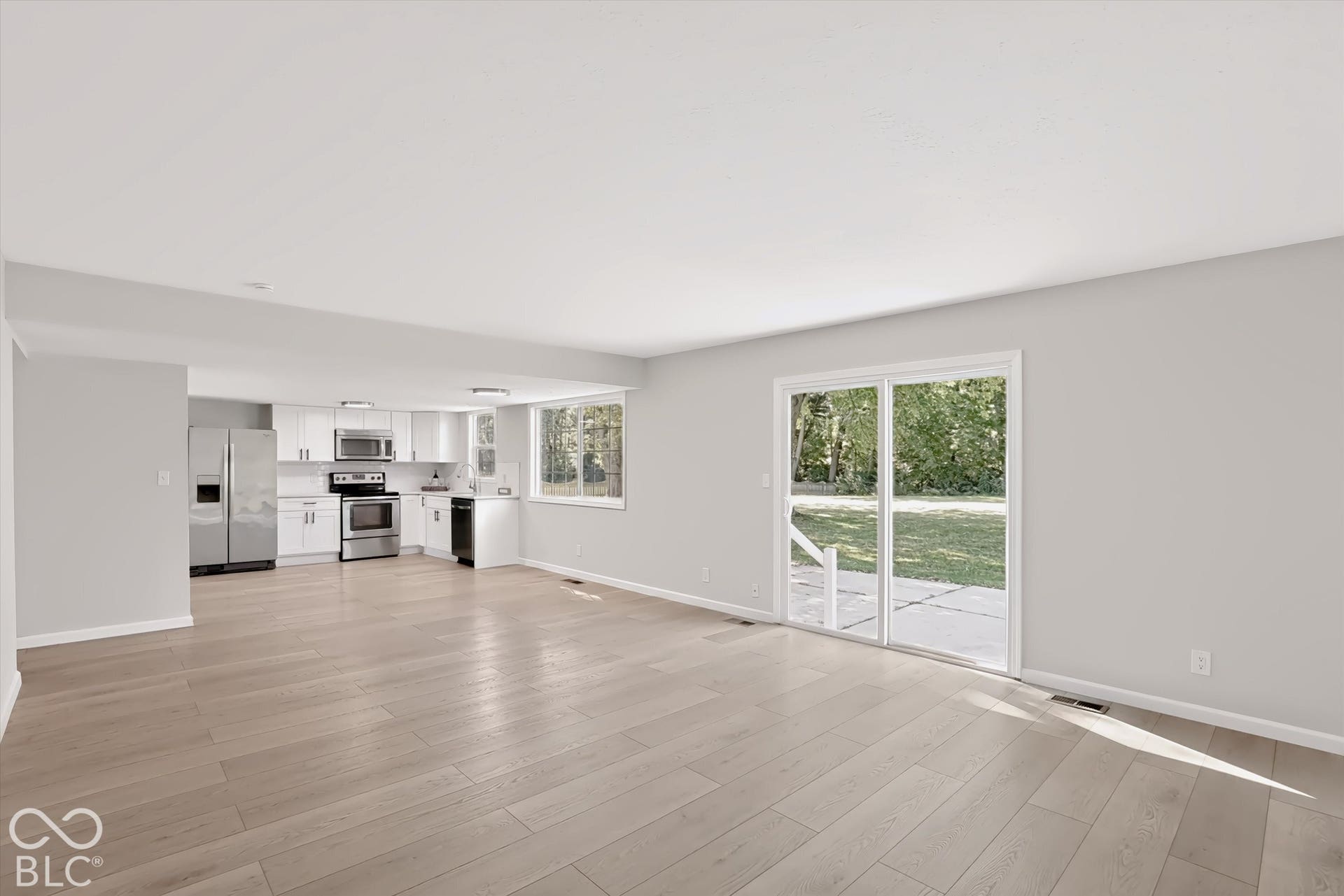 Wood-finish flooring throughout, kitchen with white cabinetry and stainless steel appliances, and a sliding glass door to the exterior