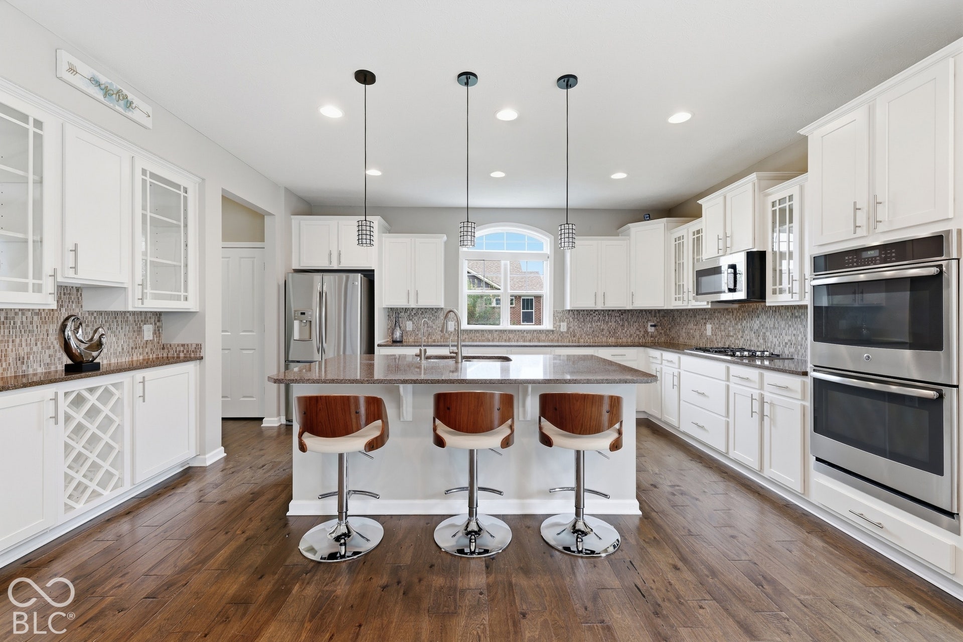 Wood-finish flooring, white cabinetry, integrated double wall ovens, built-in wine rack, and a kitchen island with pendant lighting