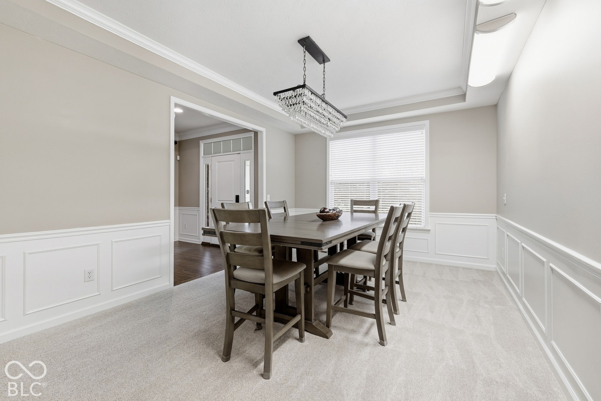 Tray ceiling with crown molding, wainscoting, recessed lighting, and a crystal chandelier