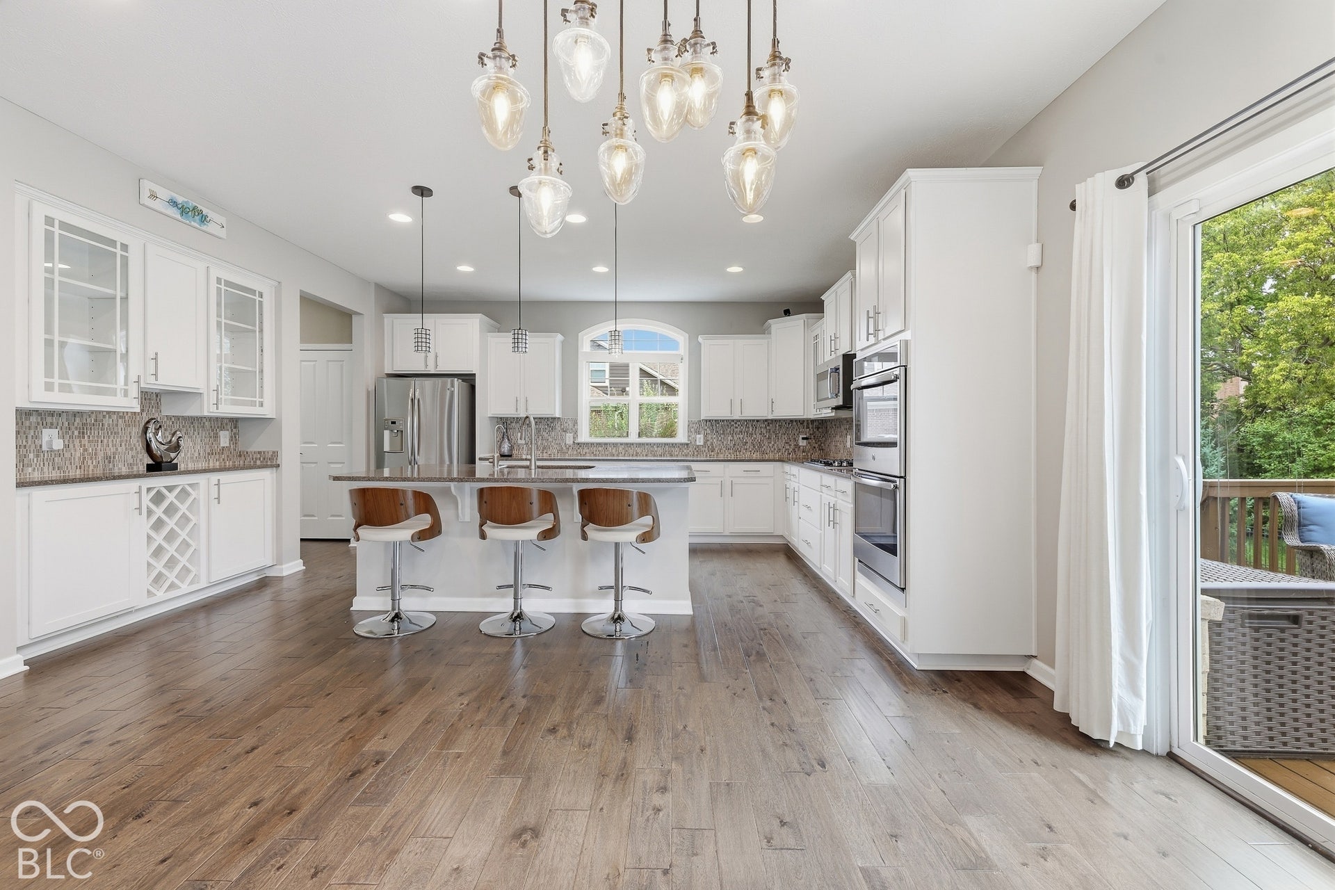 Open concept kitchen with wood-finish flooring, white cabinetry, a center island with seating, stainless steel appliances, and a sliding glass door leading to an outdoor deck