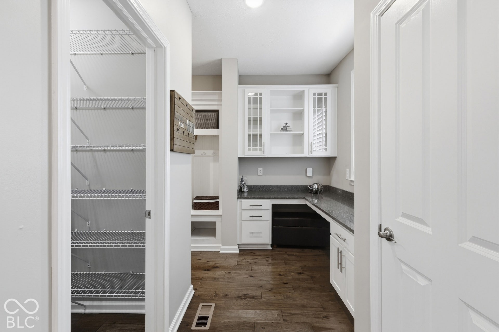 large walk-in pantry with wire shelving, wood-finish flooring, built-in white cabinetry, built-in shelving, and granite countertops
