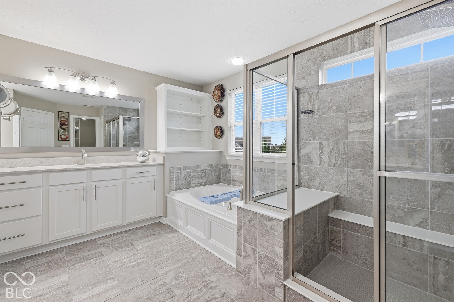 Dual vanity with extensive countertop space, integrated soaking tub, tiled walk-in shower with bench, glass shower enclosure, and built-in shelving