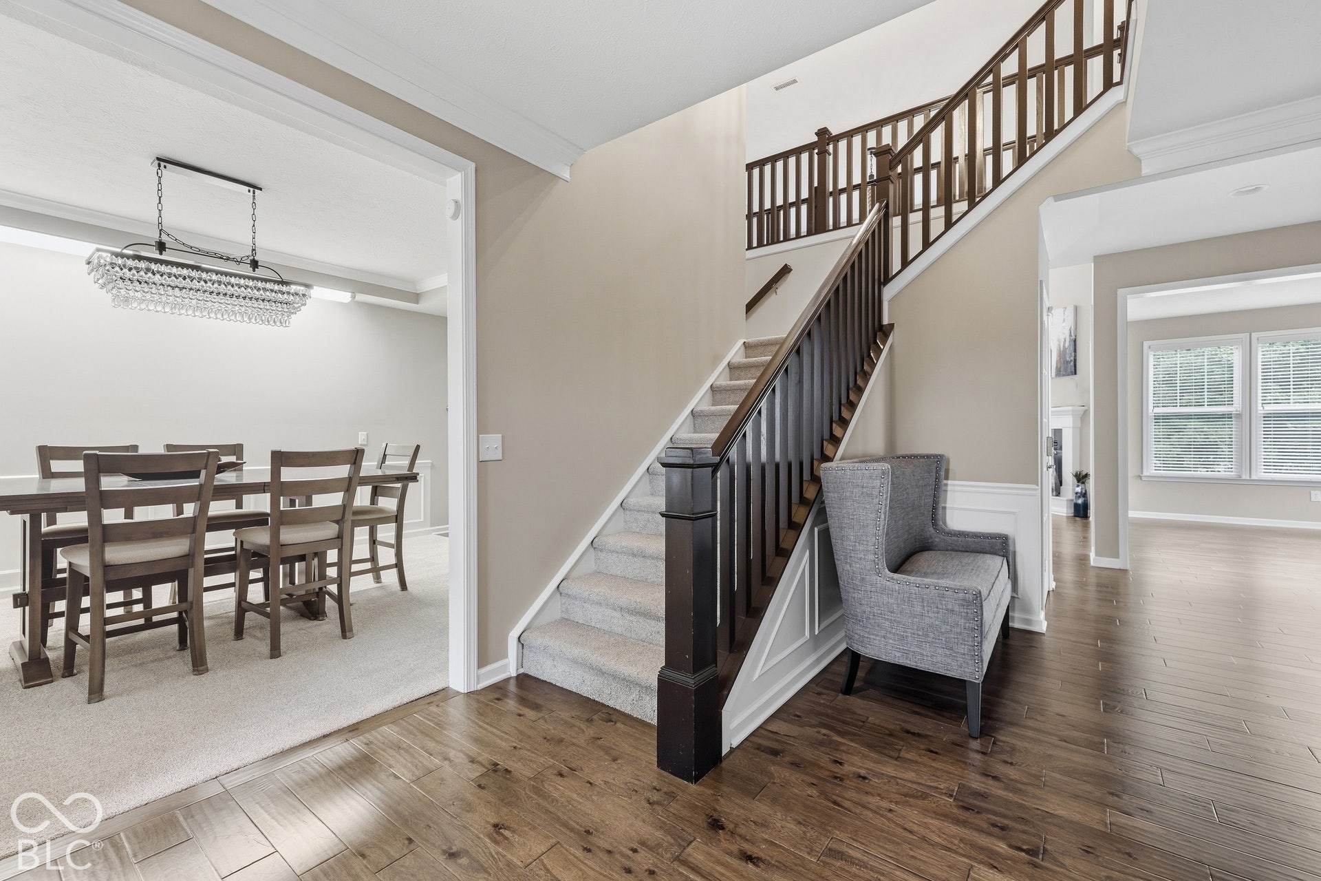Hardwood flooring extending through the main level, staircase with wood newel posts and handrails, and a newly carpeted formal room with a chandelier