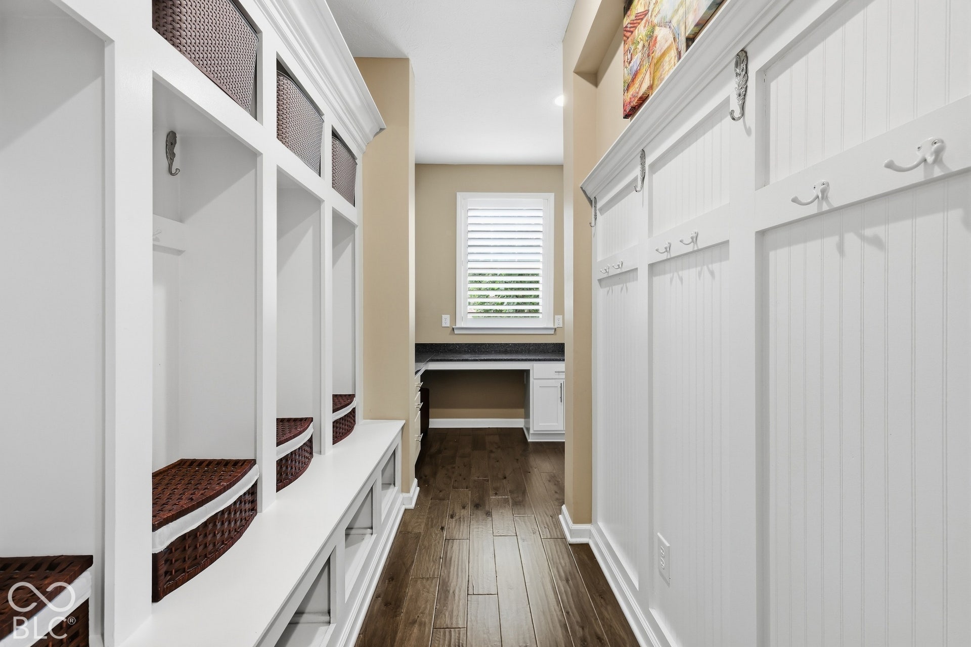 Built-in storage cubbies with bench seating, wall-mounted coat hooks, wood-finish flooring, and a dedicated workspace with a window
