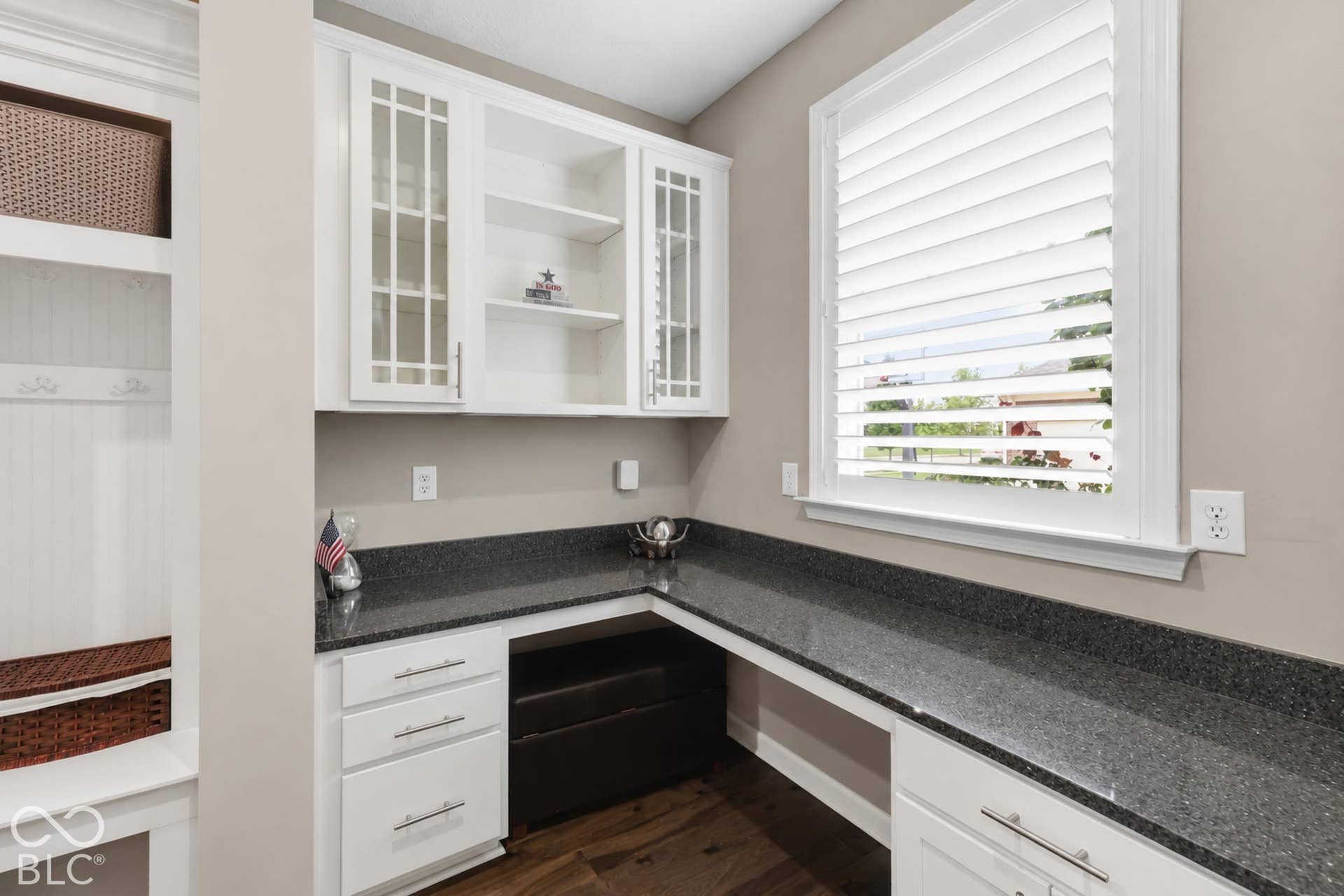 Extra planning office with white cabinetry with glass-front uppers, granite countertops, wood-finish flooring, and a built-in desk area