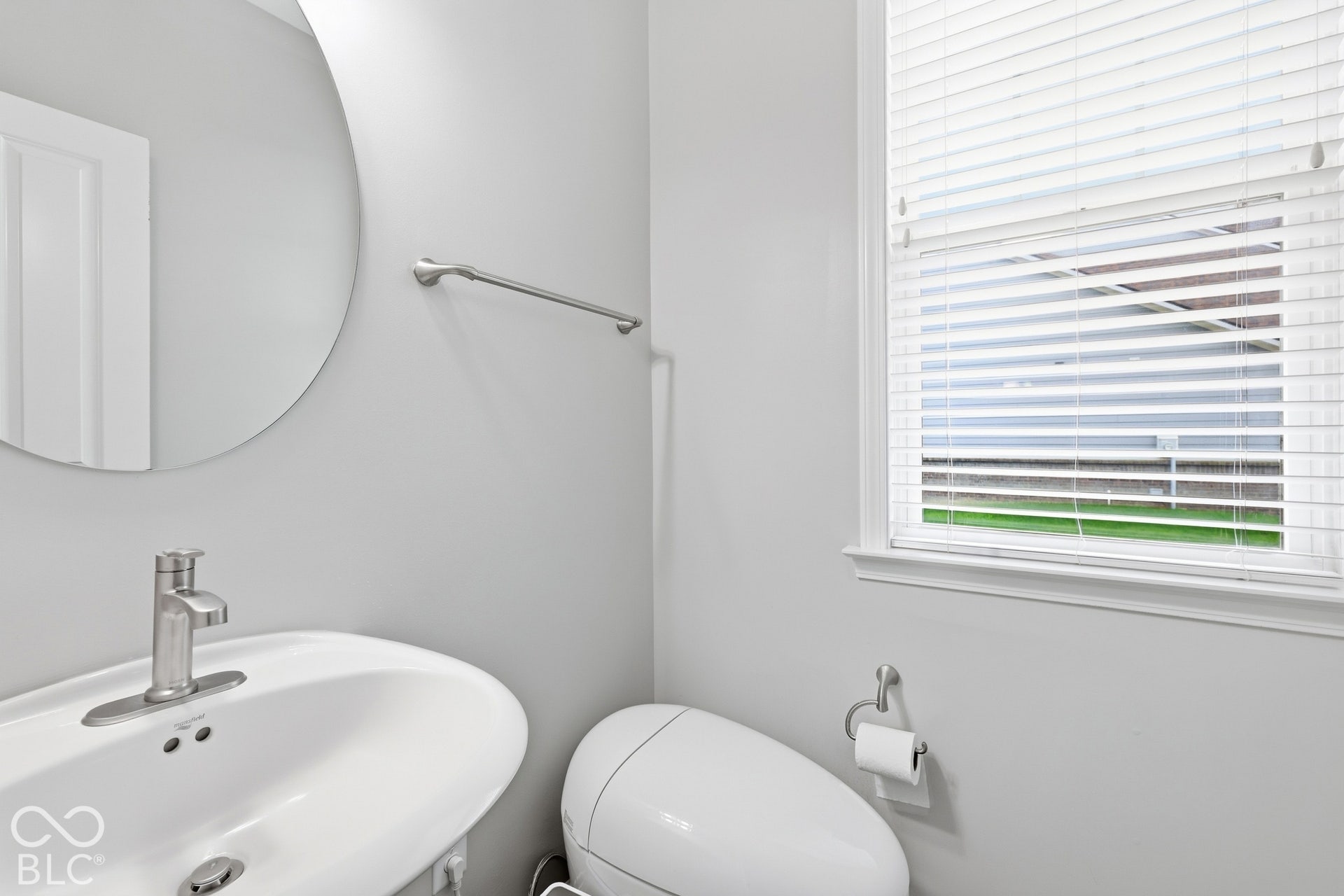 Wall-mounted oval sink with a brushed nickel faucet, round frameless mirror, and upgraded toilets throughout the home