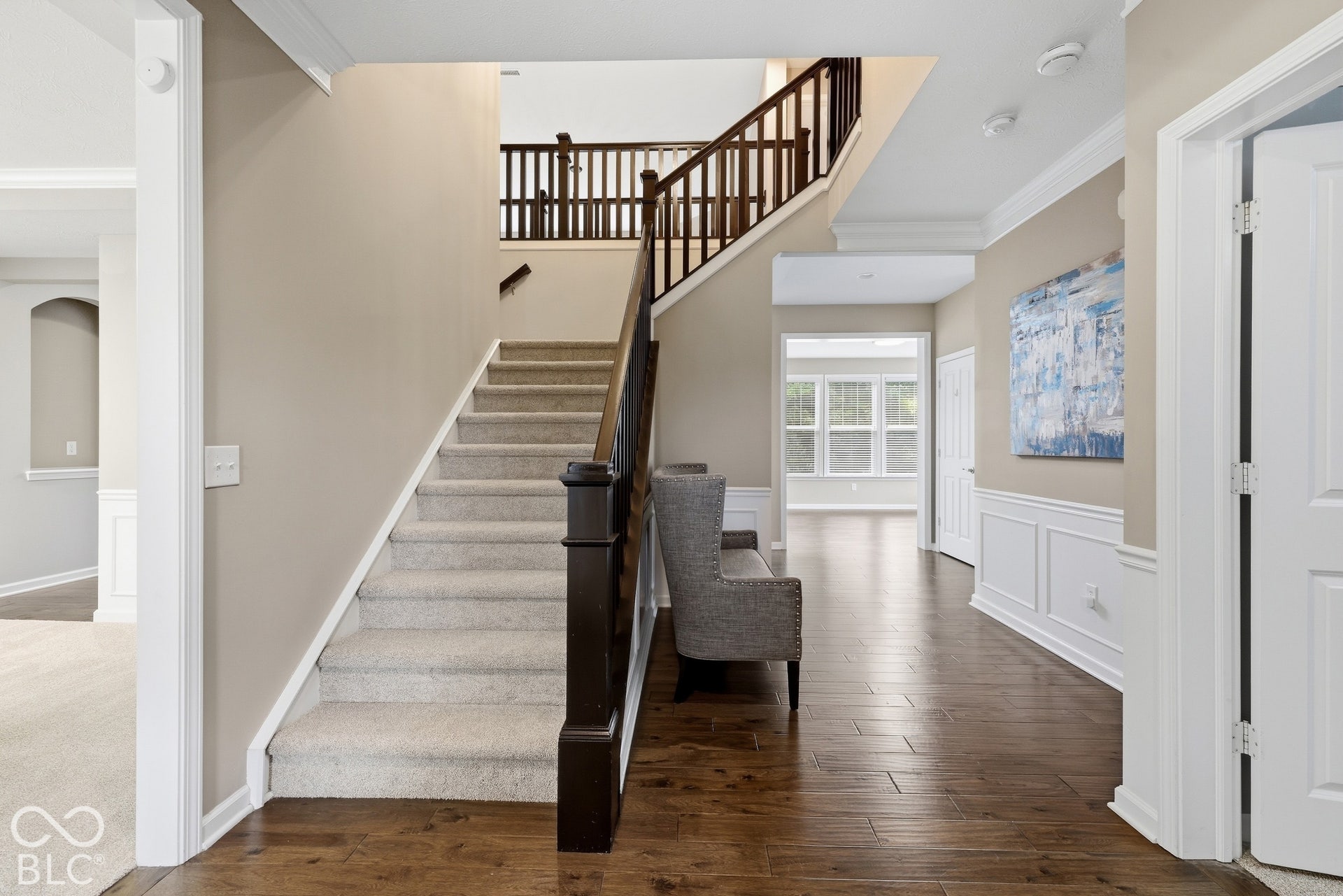 Hardwood flooring, wainscoting, crown molding, a newly carpeted staircase with wood banister, and a recessed archway