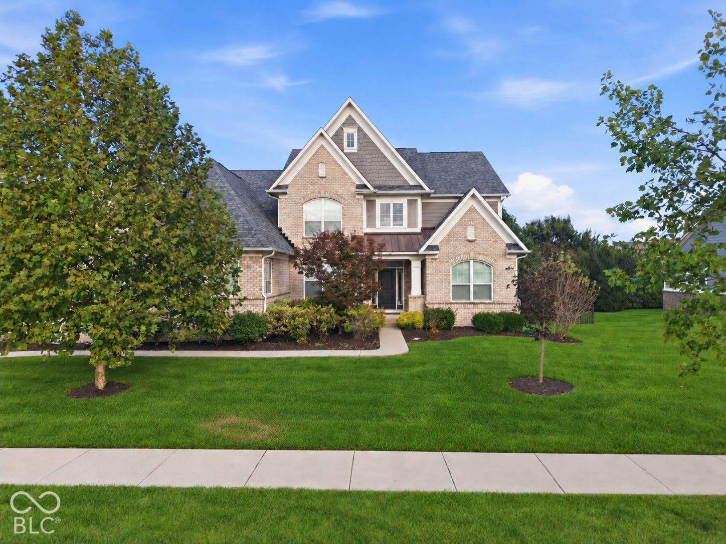 Brick and siding exterior with gabled roof lines, expansive lawn, mature trees, and concrete sidewalk