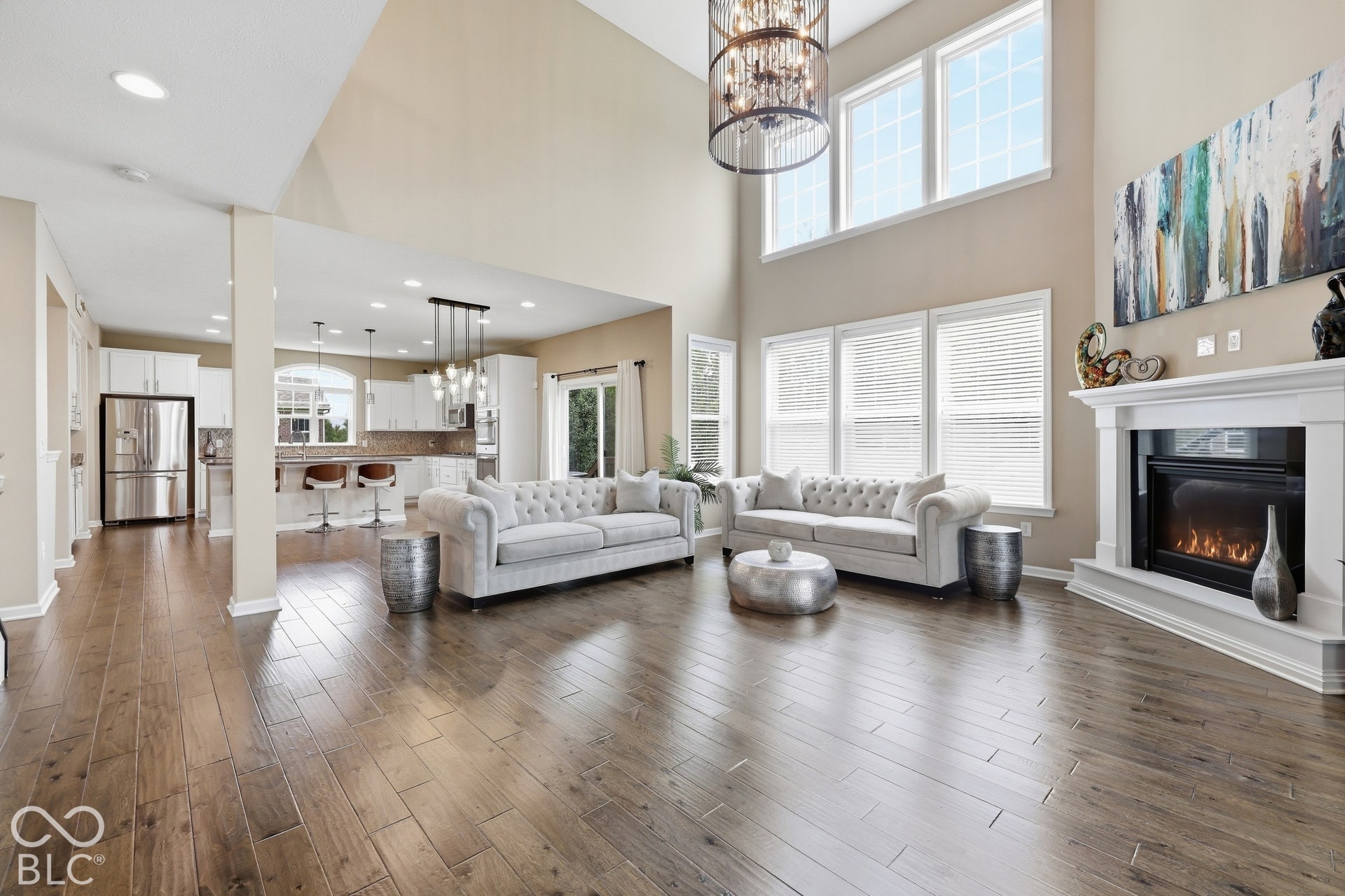 Spacious great room featuring soaring ceilings, wood-finish flooring, a cozy fireplace, and views of the private backyard.