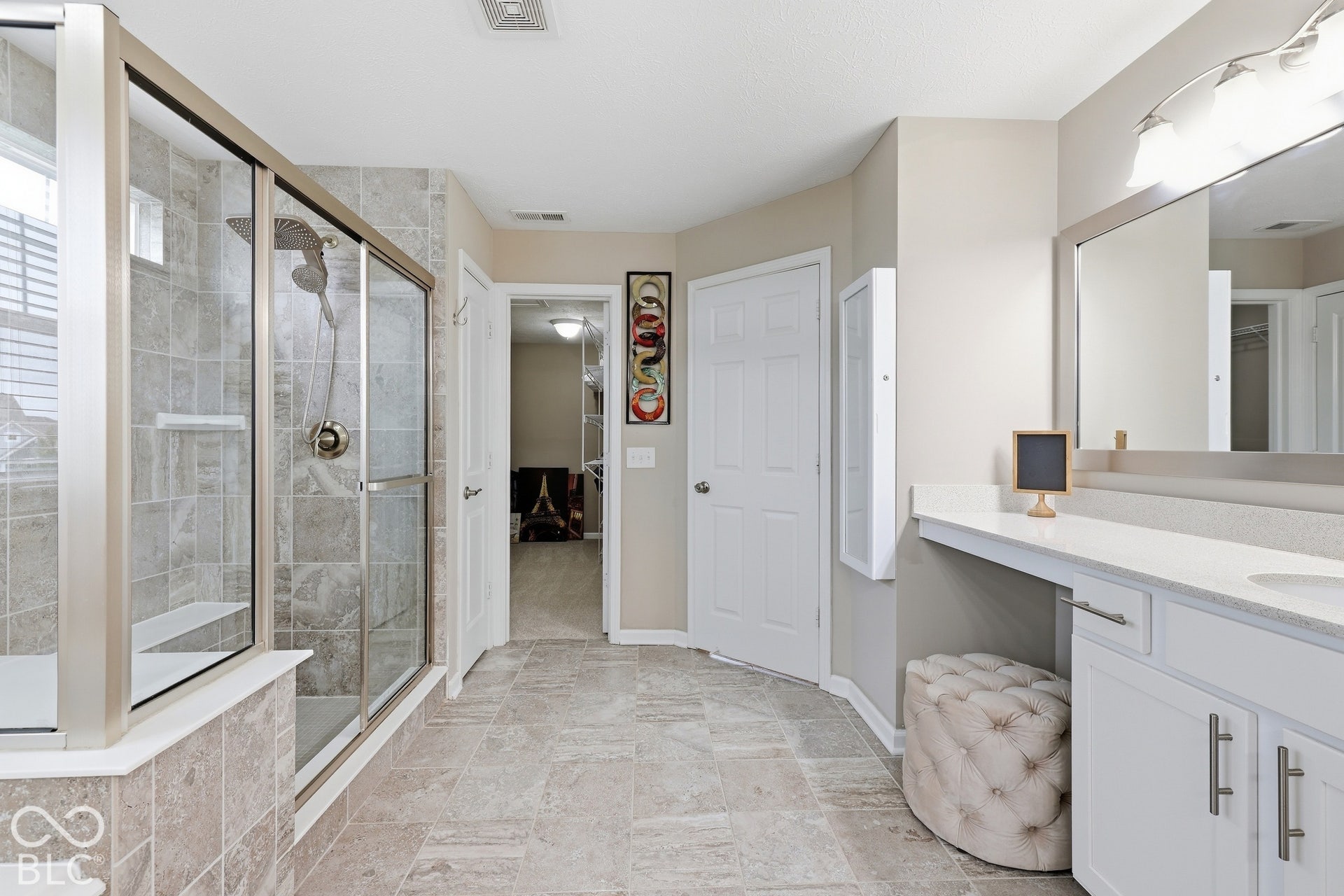Spacious bathroom featuring a glass-enclosed shower with tile surround, built-in shower bench, and a dual-sink vanity with a large mirror