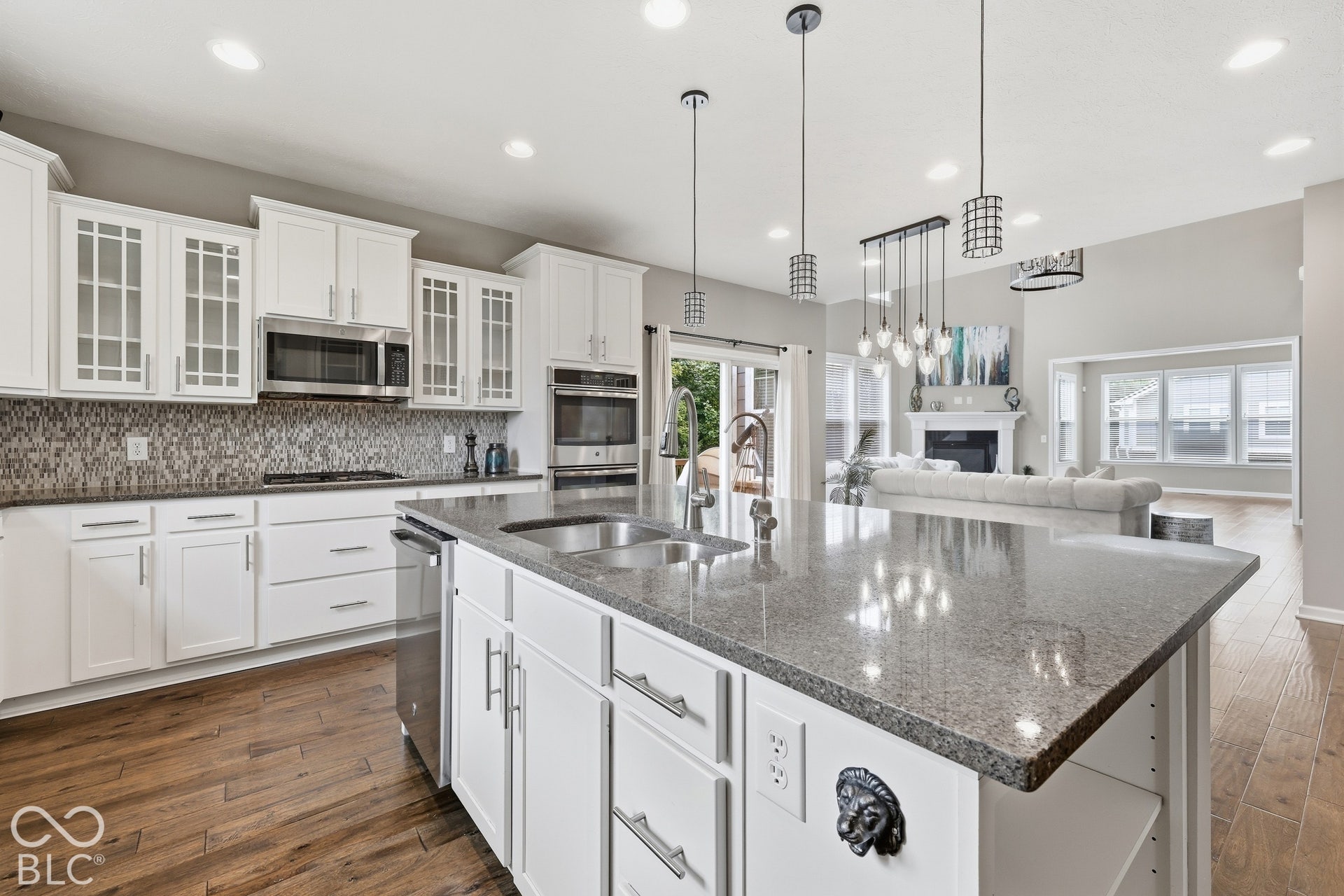 Kitchen island with a built-in sink and granite countertop, white cabinetry with glass-front accents, stainless steel appliances, and wood-finish flooring