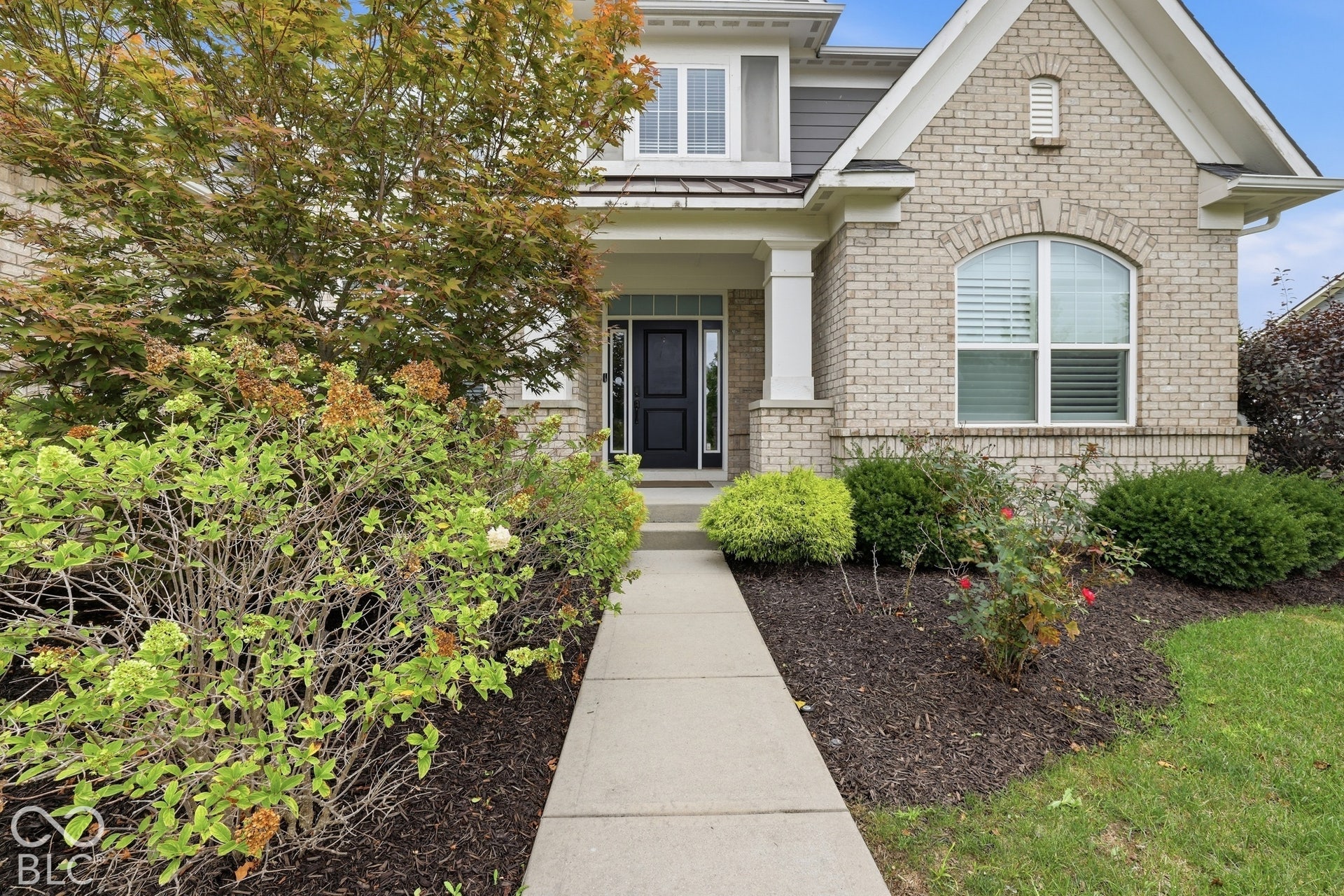 Brick and siding exterior with an arched window, covered porch, and concrete walkway