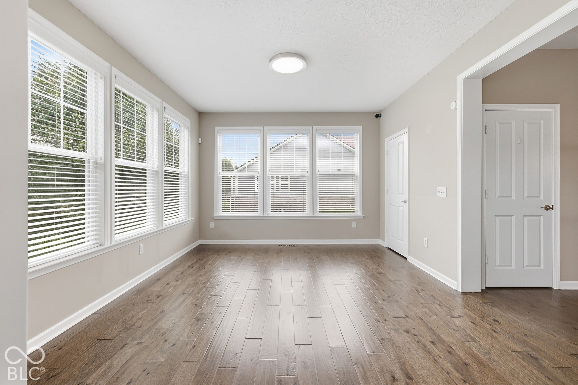 Wood-finish flooring with white trim and multiple windows featuring blinds