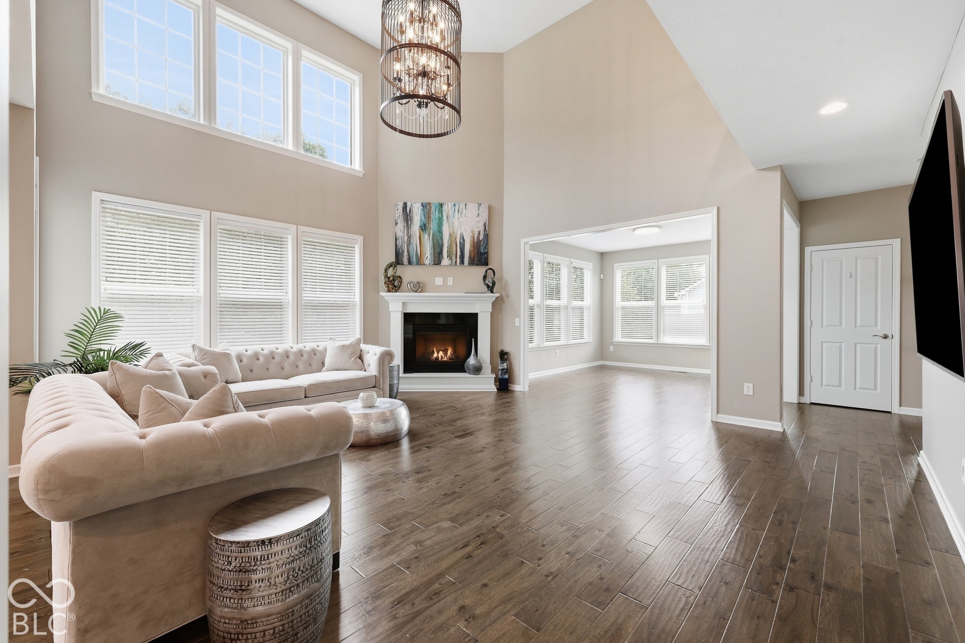 Vaulted ceiling, wood-finish flooring, white fireplace with mantle, multiple windows, and a tiered chandelier