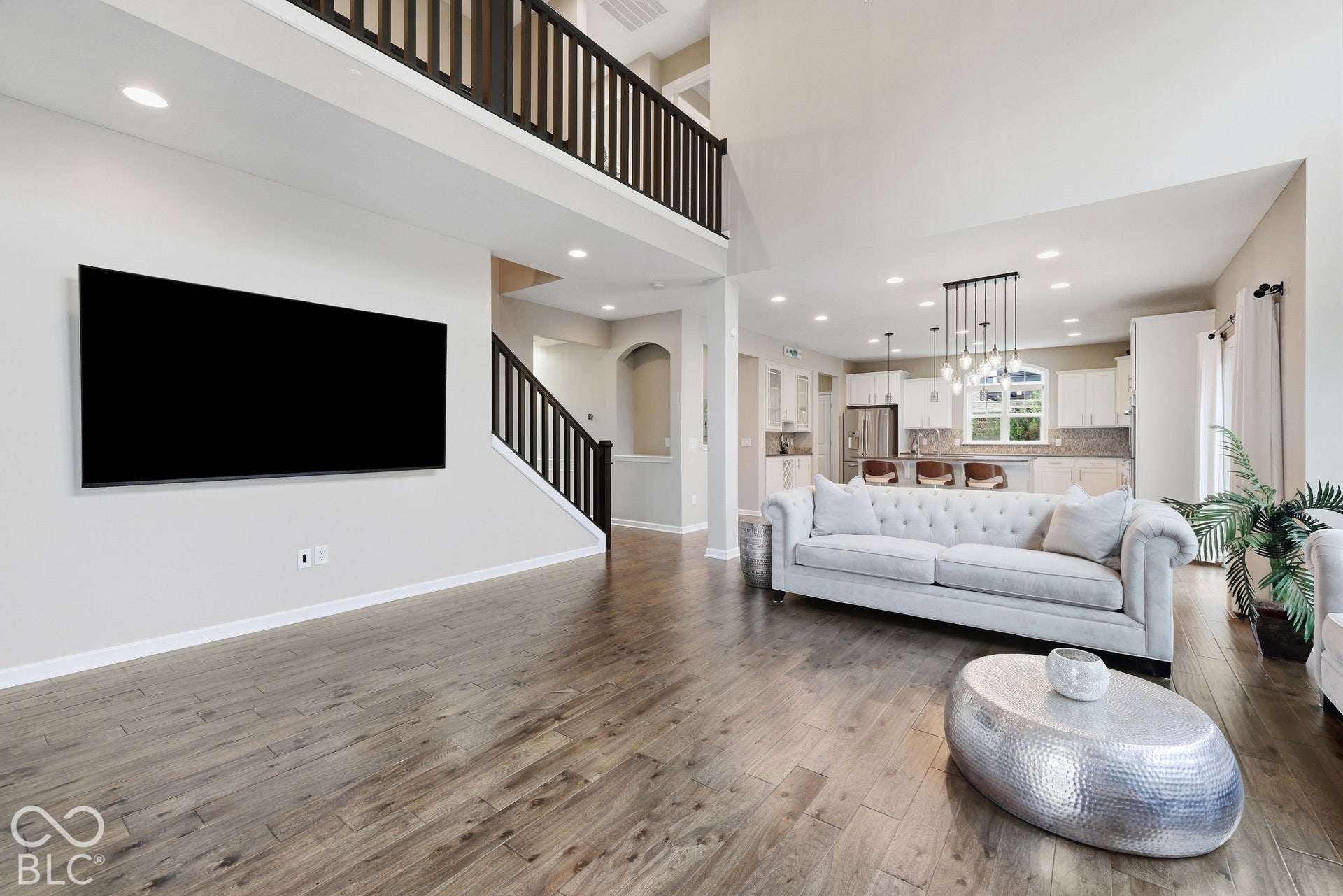 Spacious Great Room offering soaring ceilings, wood-finish flooring, cozy fireplace and private tree-lined view of the backyard