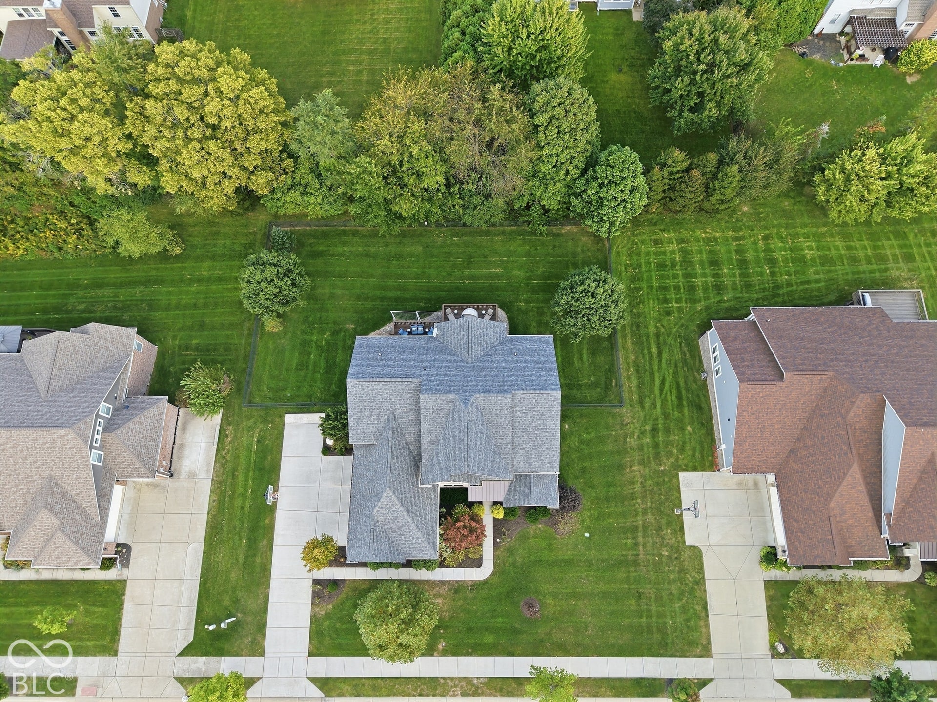 Gable roofline, concrete driveway, concrete sidewalks, mature trees, and landscaping