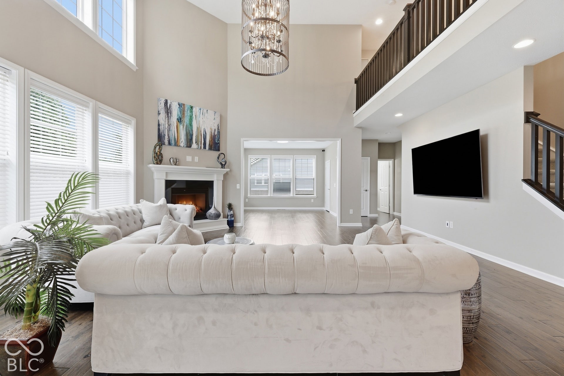 Two-story great room featuring a cozy fireplace with a mantel, wood-finish flooring, and a large chandelier
