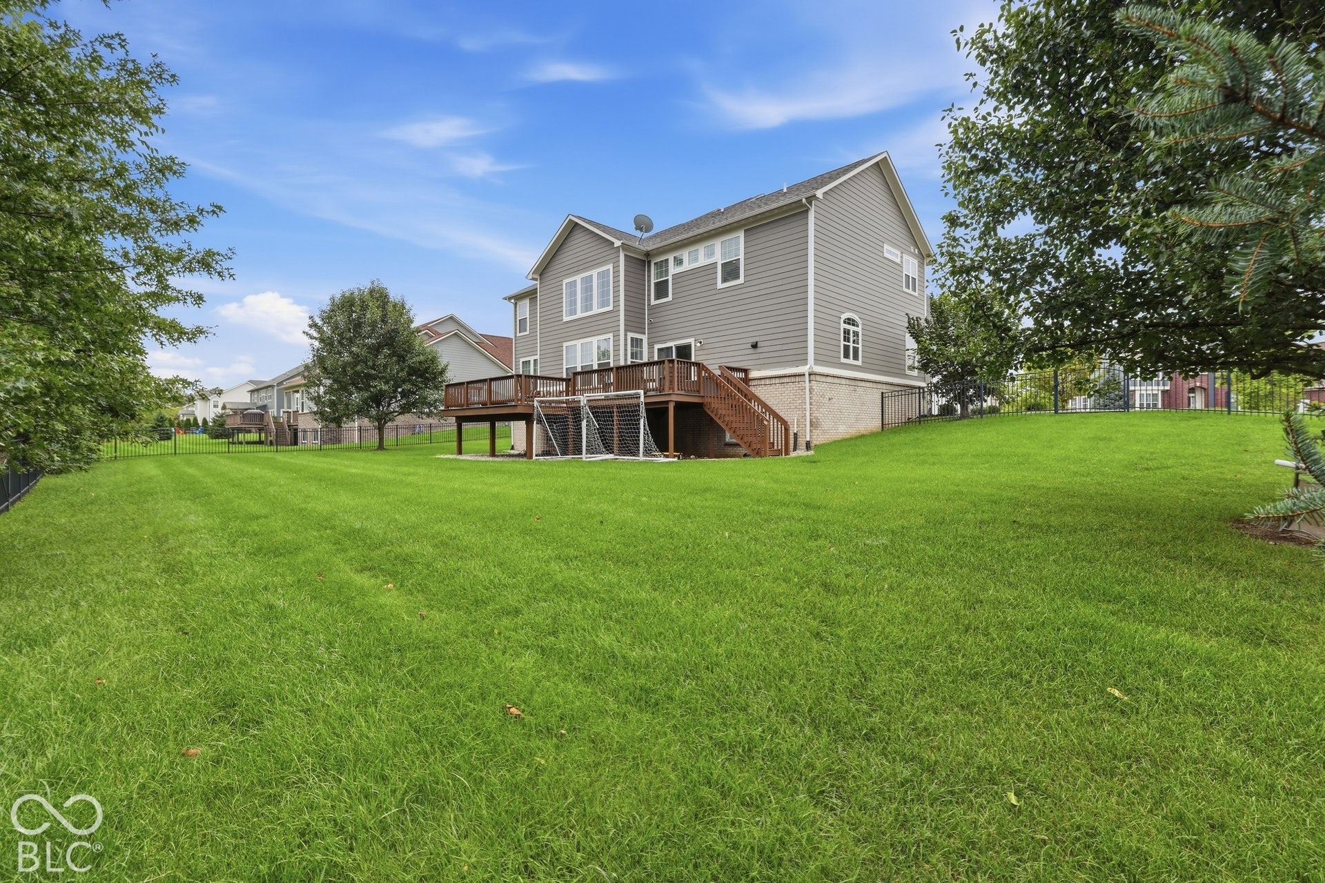 Expansive rear yard featuring a large wooden deck, fenced yard, and sprinkler system