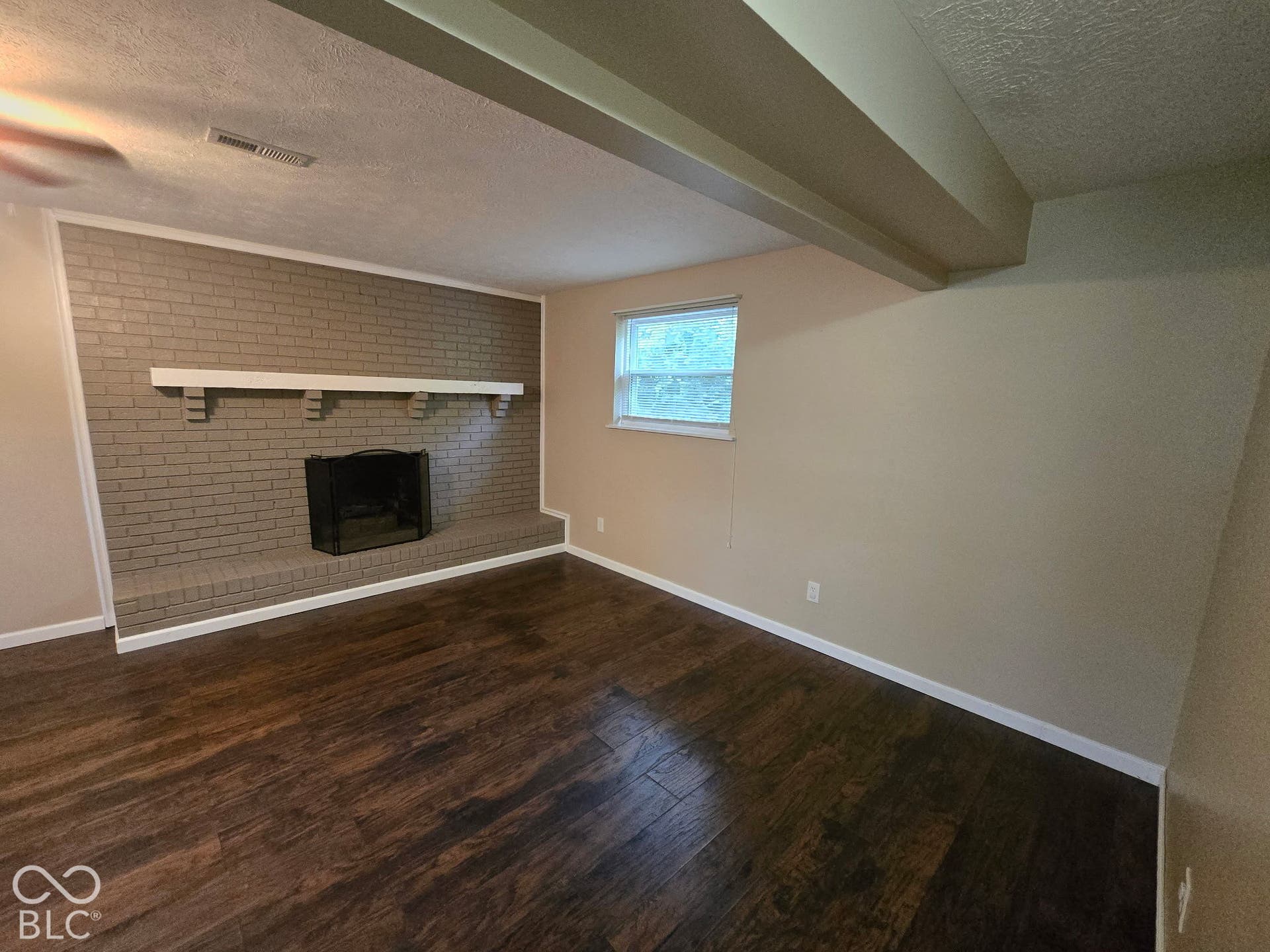 Warm wood-finish flooring complements a brick accent wall with a white mantel and hearth