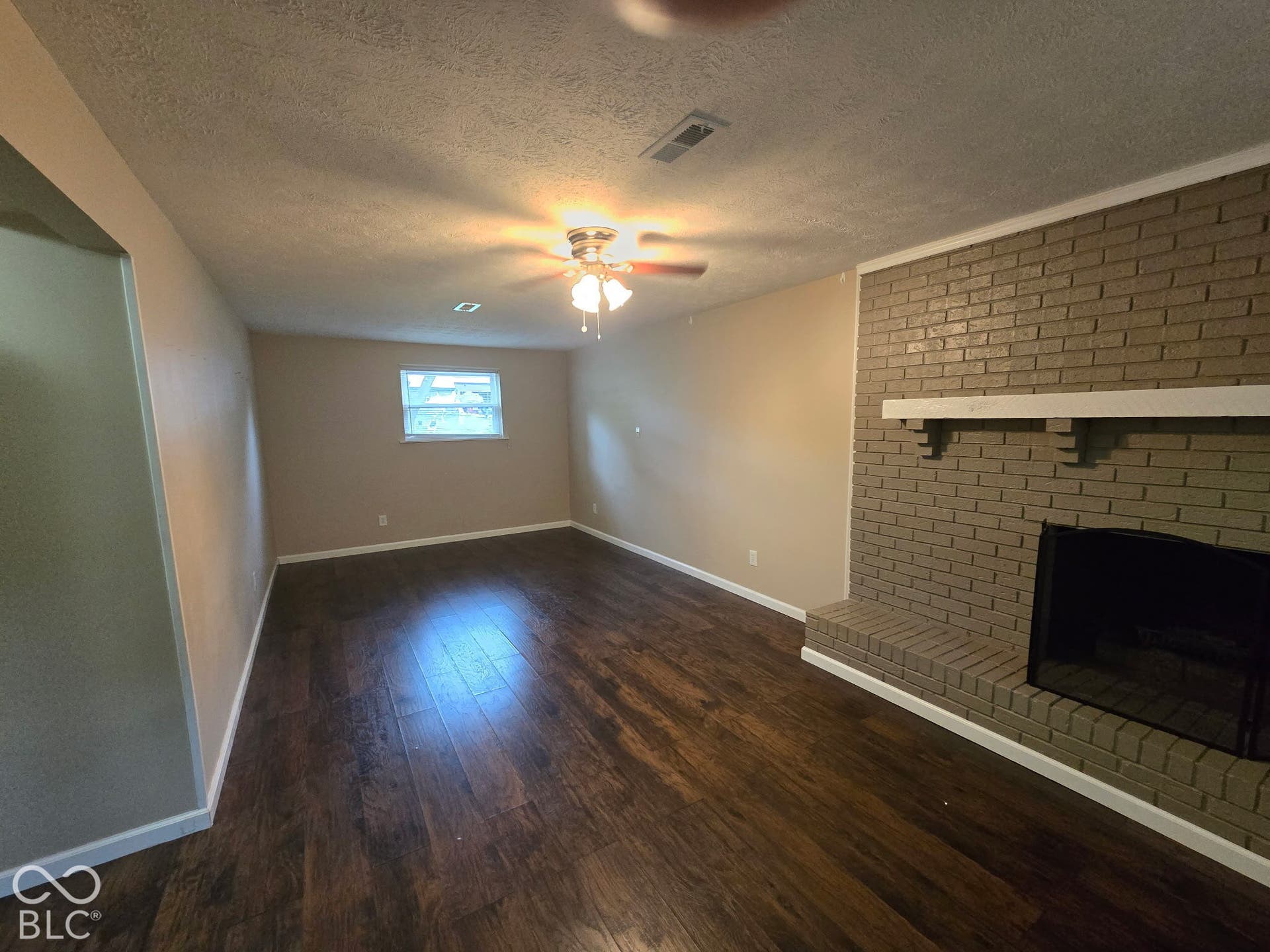 Expansive room featuring wood-finish flooring, a brick fireplace with a hearth, a mantel, and a ceiling fan