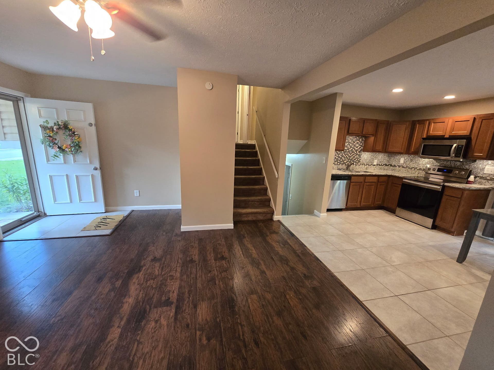 Wood-finish flooring, staircase with carpeted treads, kitchen with wood cabinetry, tile backsplash, and stainless steel appliances