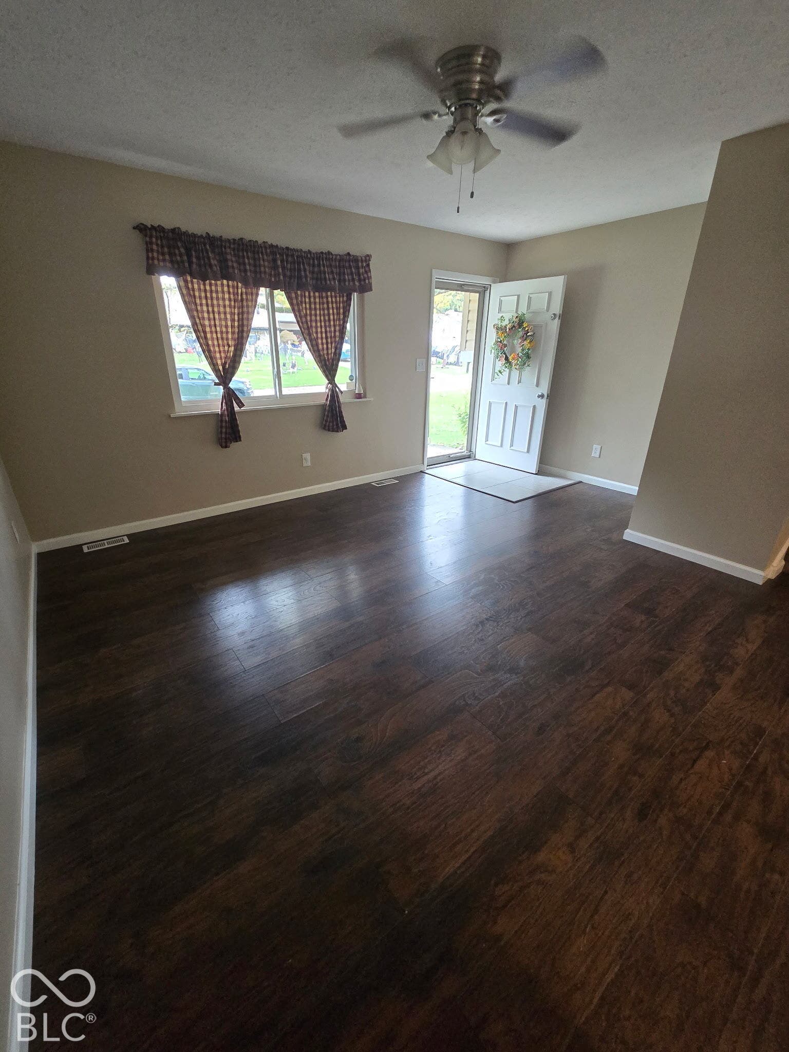 Wood-finish flooring throughout, ceiling fan with integrated lighting, and a white paneled entry door