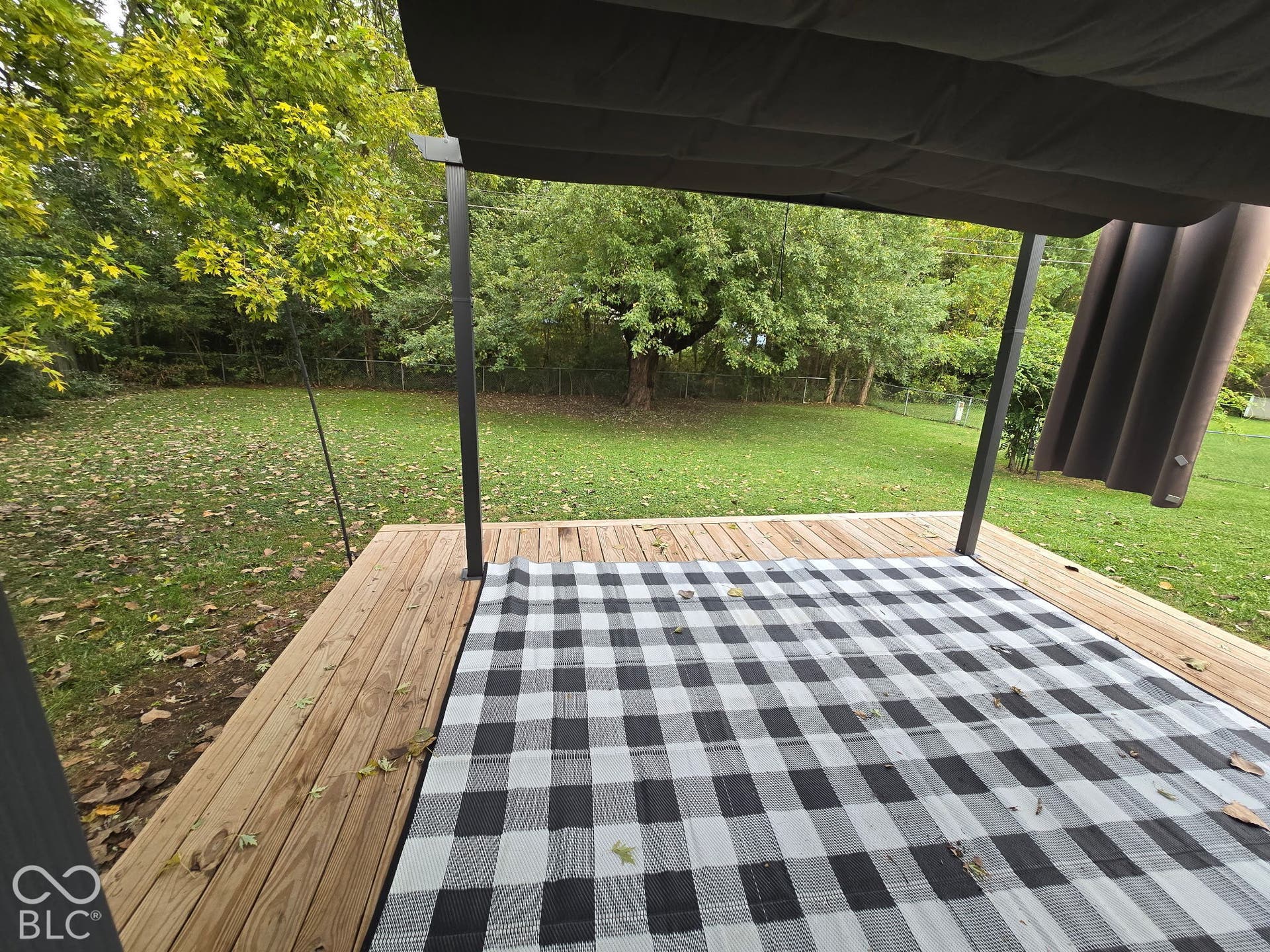 Expansive green lawn with mature trees and a wood-finish deck featuring a black fabric canopy