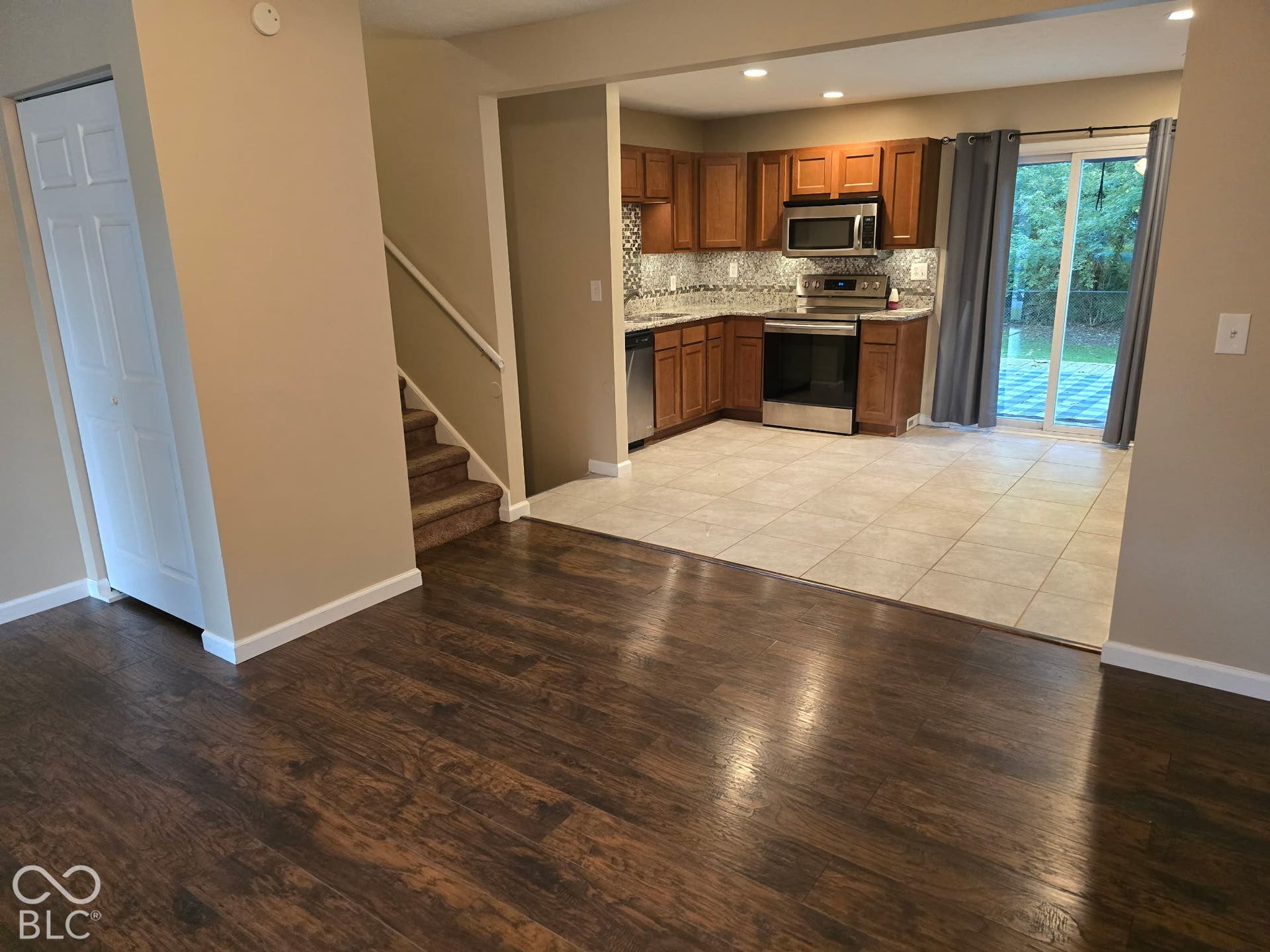 Wood-finish flooring, staircase with carpeted treads, kitchen with wood-finish cabinetry, stainless steel appliances, and a tiled floor